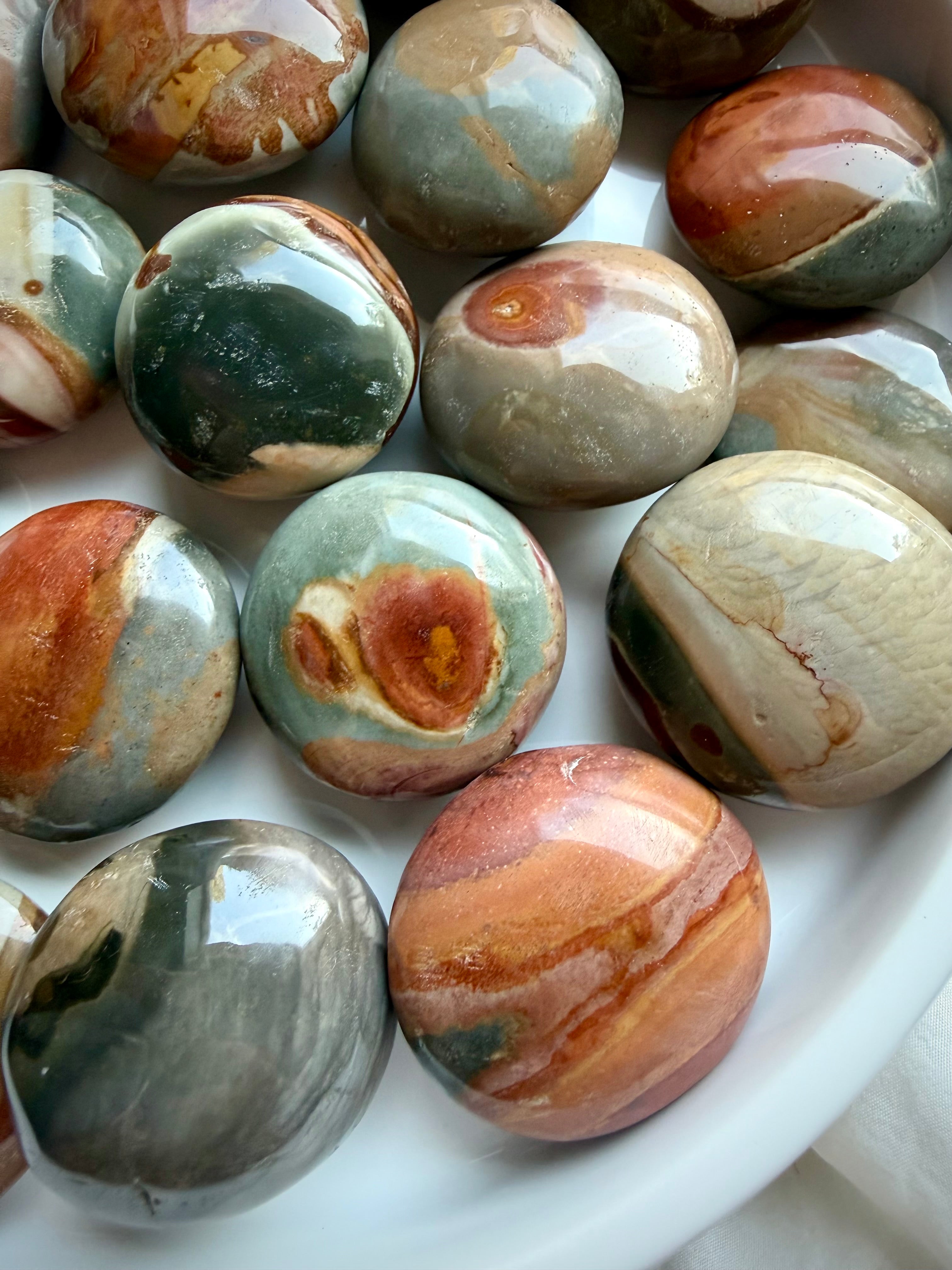 Close-up of polished Polychrome Jasper pocket stones with colorful earthy swirls, natural banding, and rounded shapes