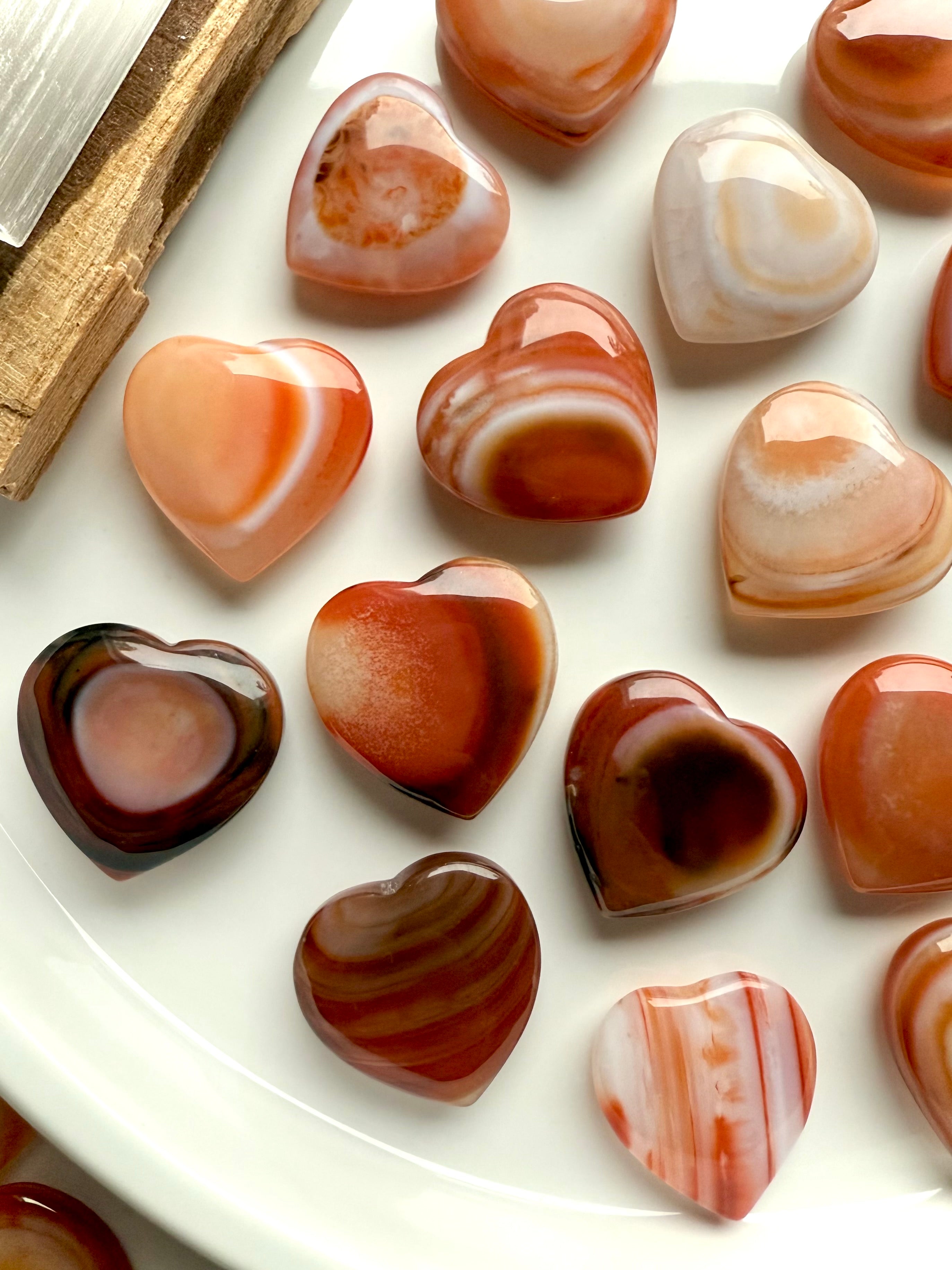 Mini Carnelian heart crystals showing natural banding and warm orange tones, sacral chakra stones for creativity, joy, and motivation