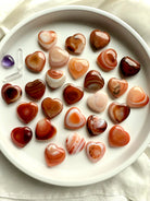 Assorted mini Carnelian heart carvings with rich orange, red, and cream banding, polished sacral chakra crystals for joy and inspired action