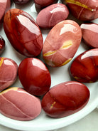 glossy Mookaite Jasper palm stones with natural cream and crimson patterns for root chakra grounding and vitality