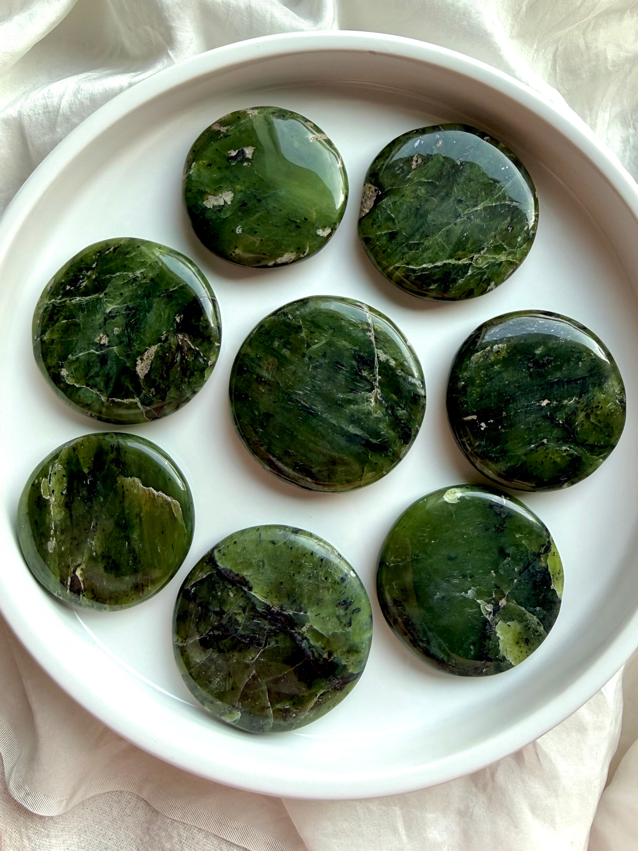 Nephrite jade palm stones arranged in white bowl, dark green heart chakra crystals for meditation, grounding, and protection