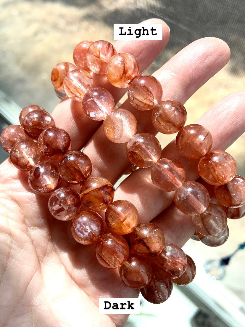 Four Hematoid Quartz bracelets in hand, showing two light and two dark Fire Quartz styles labeled for comparison