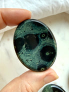 Kambaba Jasper worry stone held in hand with deep green and black orbicular patterns, a grounding crystal for emotional balance