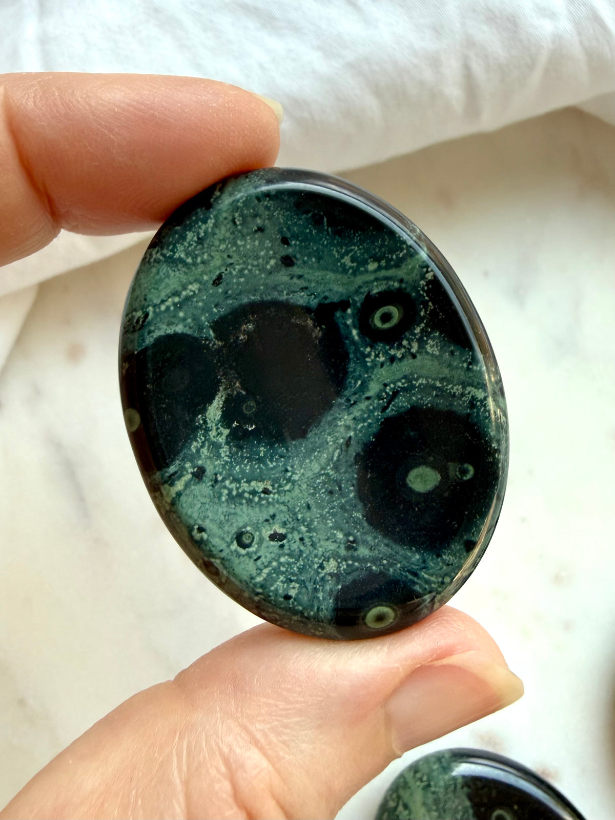 Kambaba Jasper worry stone held in hand with deep green and black orbicular patterns, a grounding crystal for emotional balance