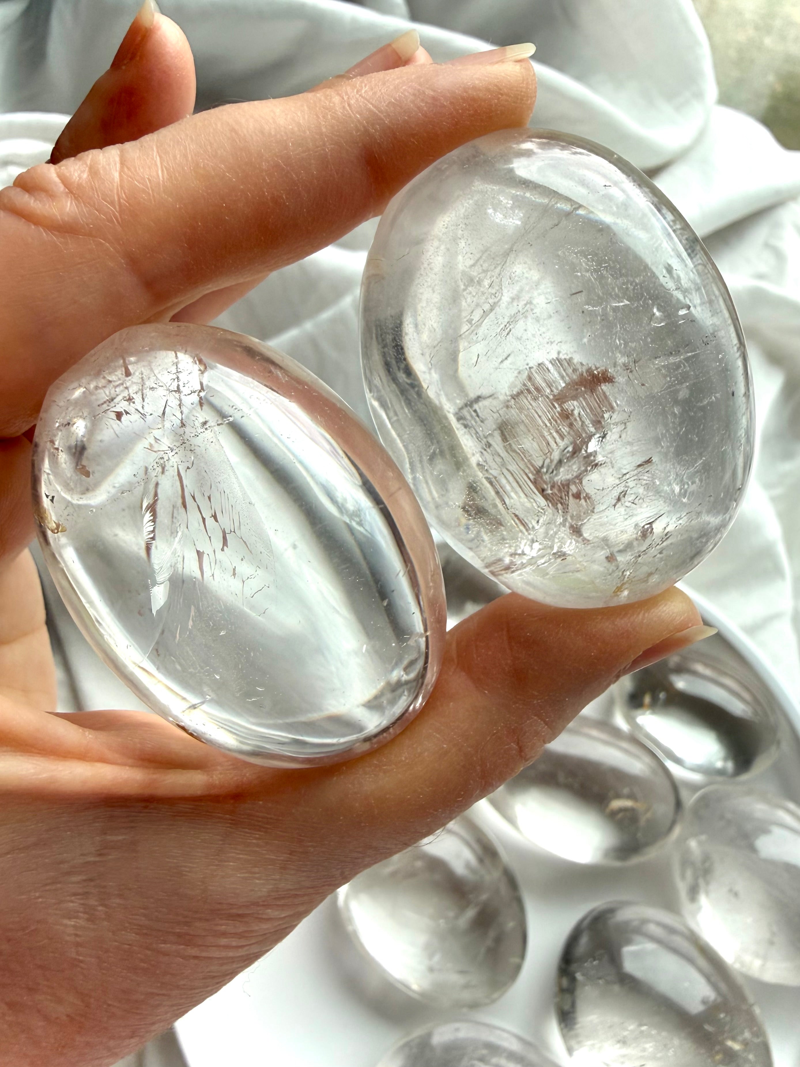 Two clear quartz palm stones close up, held to the light showing high clarity, internal veils & flashes