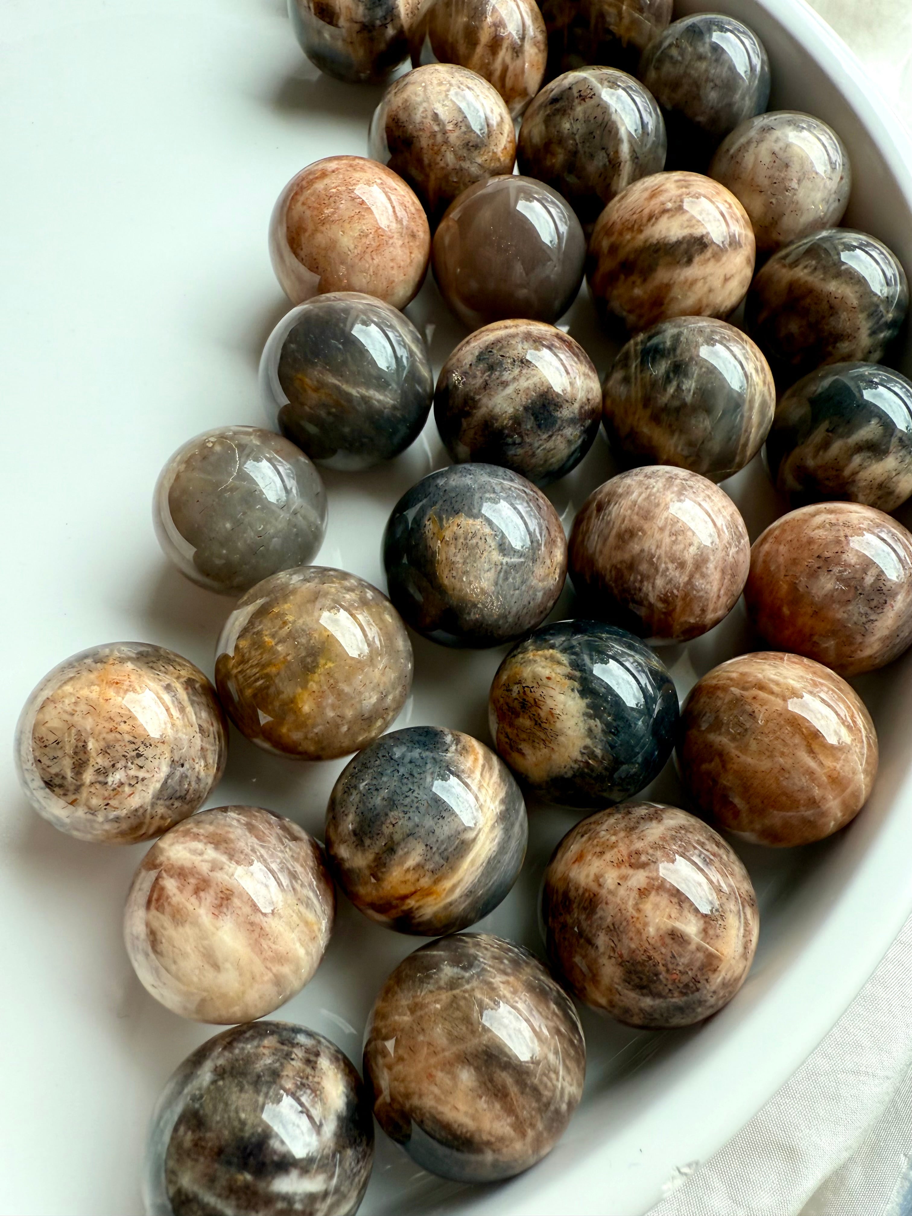 Mini Black Moonstone spheres on a white plate, showing dark shimmer & subtle flash — crystals for intuition, grounding, & feminine energy