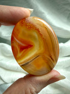 Golden-orange Carnelian worry stone held in hand with translucent Agate banding for creativity and Sacral Chakra healing