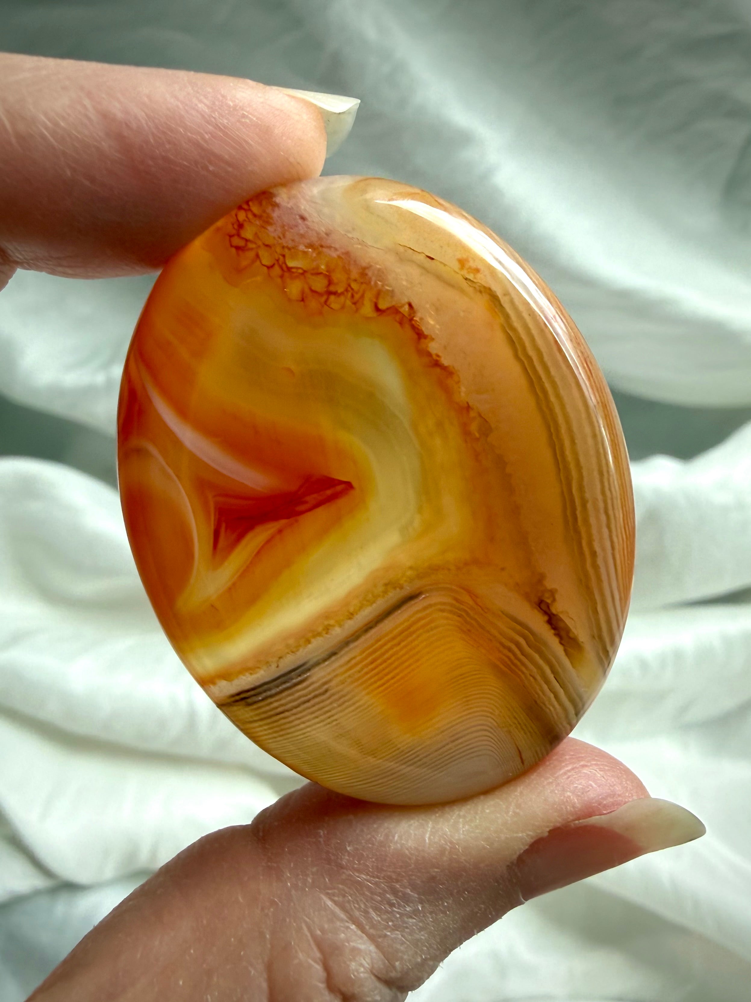 Golden-orange Carnelian worry stone held in hand with translucent Agate banding for creativity and Sacral Chakra healing
