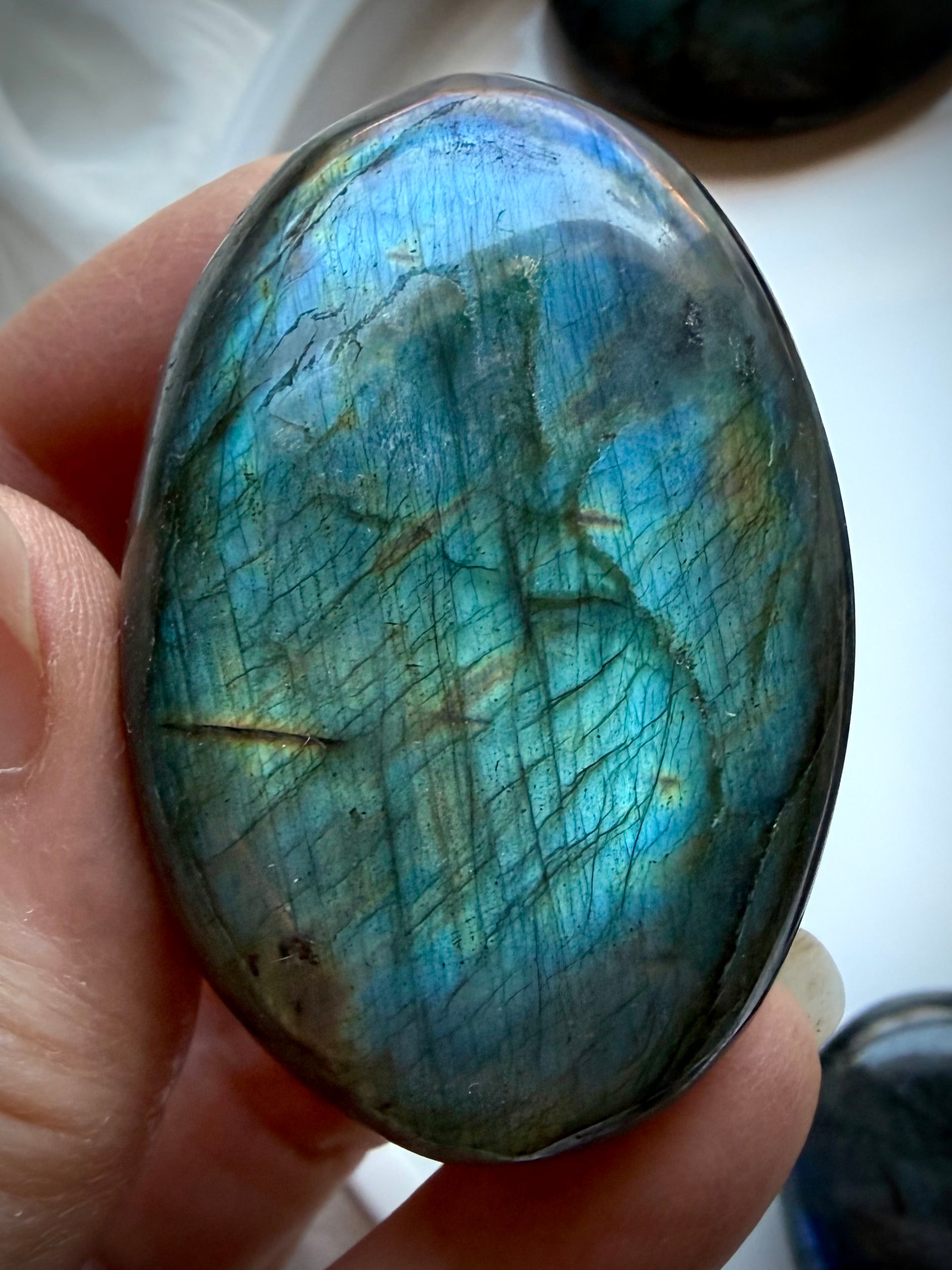 Teal flash Labradorite palm stone held in hand with vivid labradorescence and polished natural crystal finish