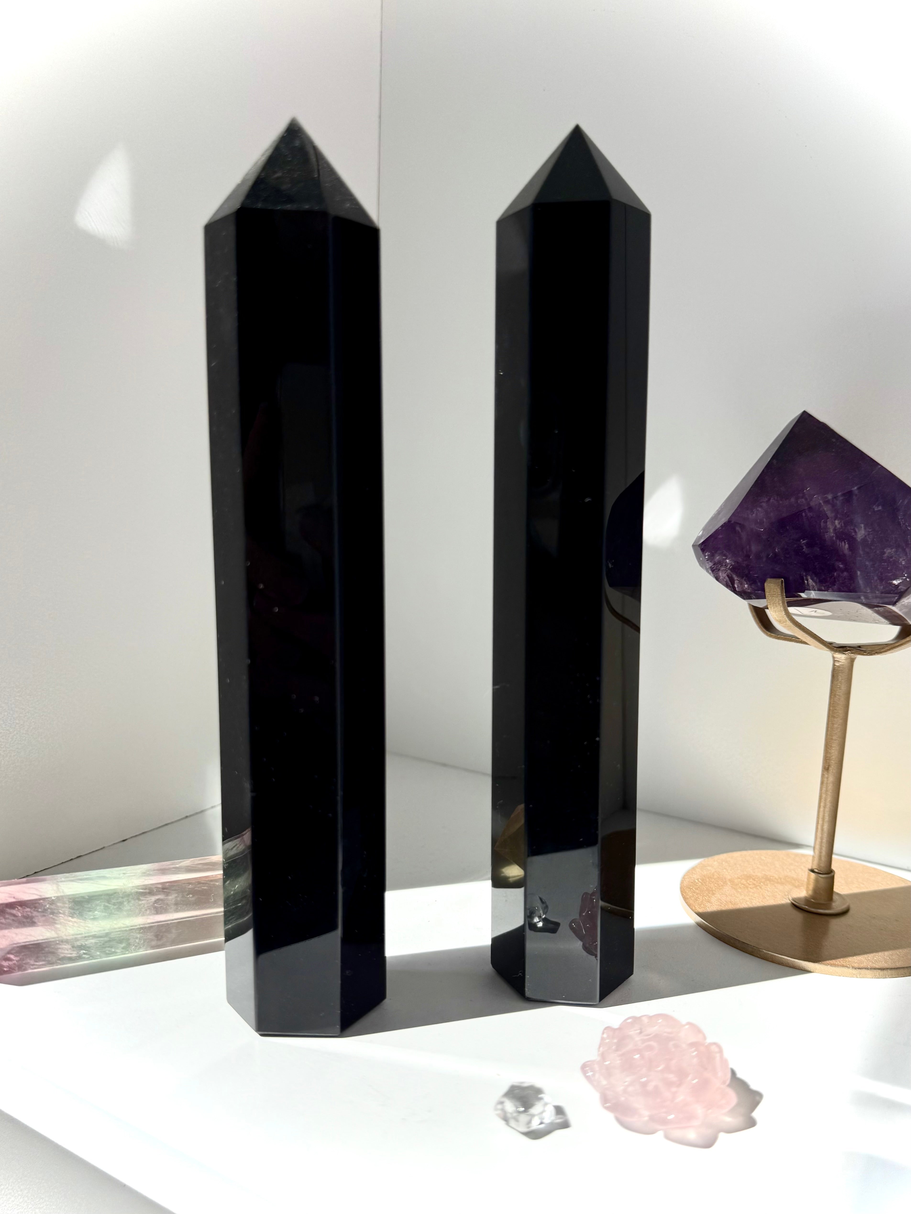 Two large Black Obsidian towers standing on a white shelf with other crystals — protective stones for home energy clearing.