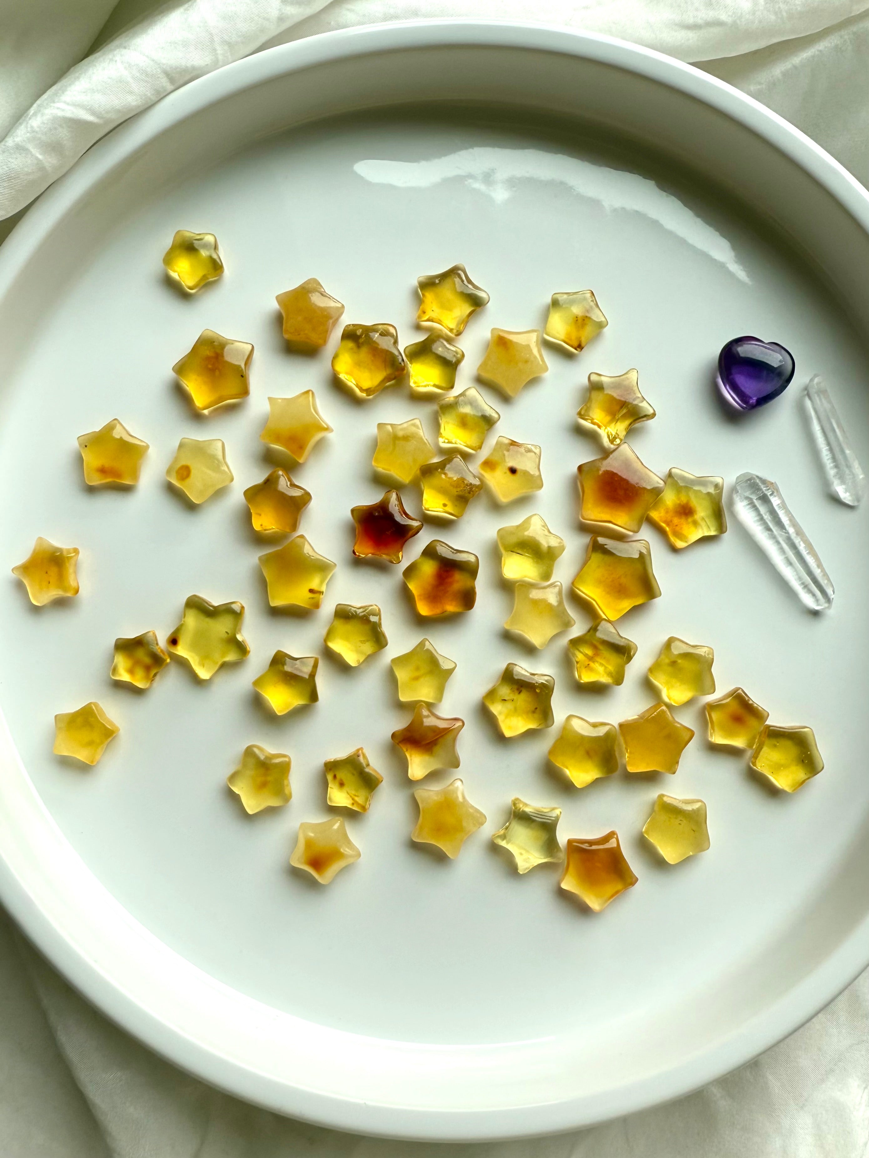 Mini Amber Star carvings reflecting light on white background – crystal stars for joy, empowerment, and chakra balance