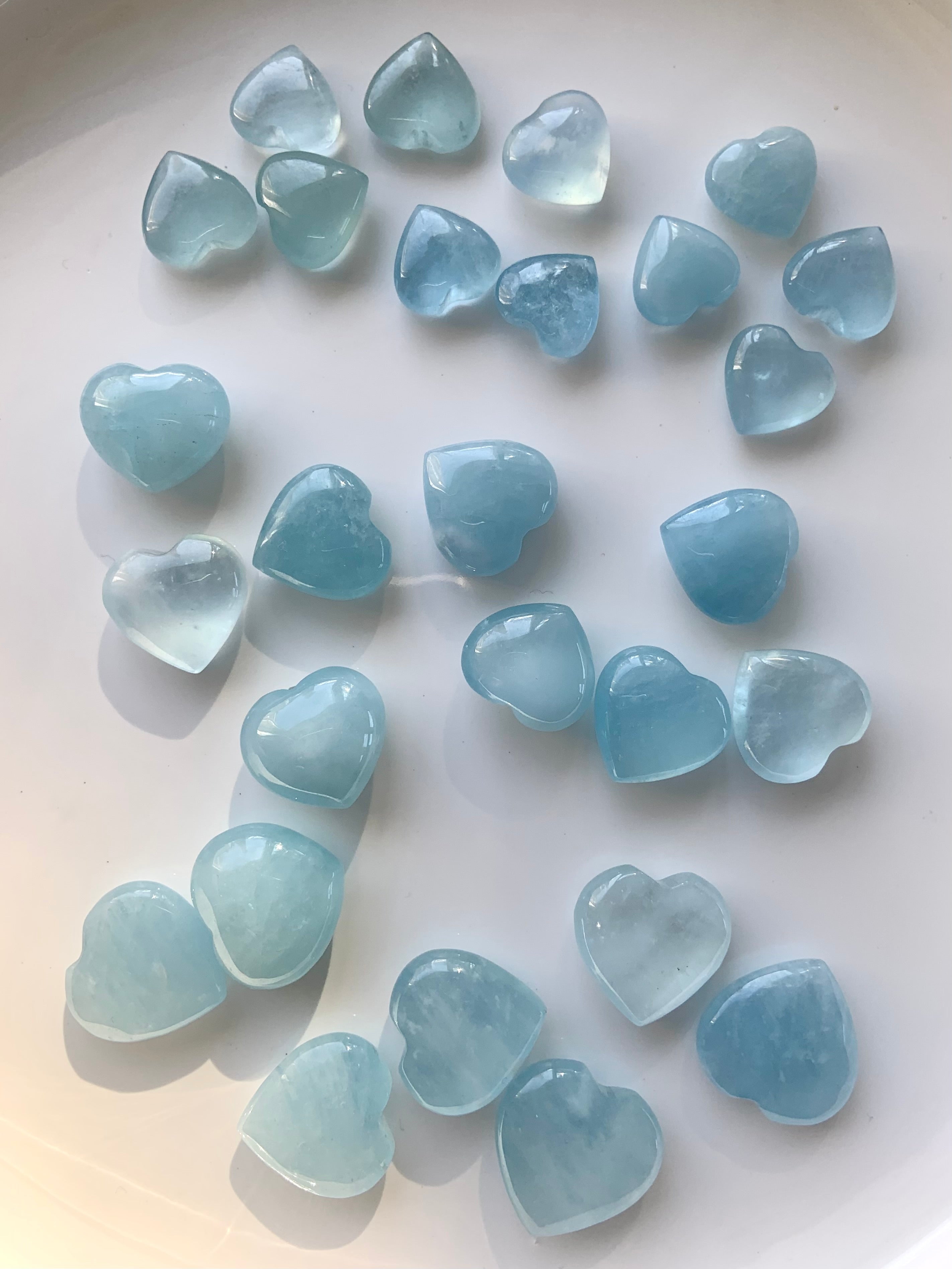 Array of Aquamarine hearts organized by size on a white surface — crystal heart carving collection in tranquil blue tones for throat chakra support.