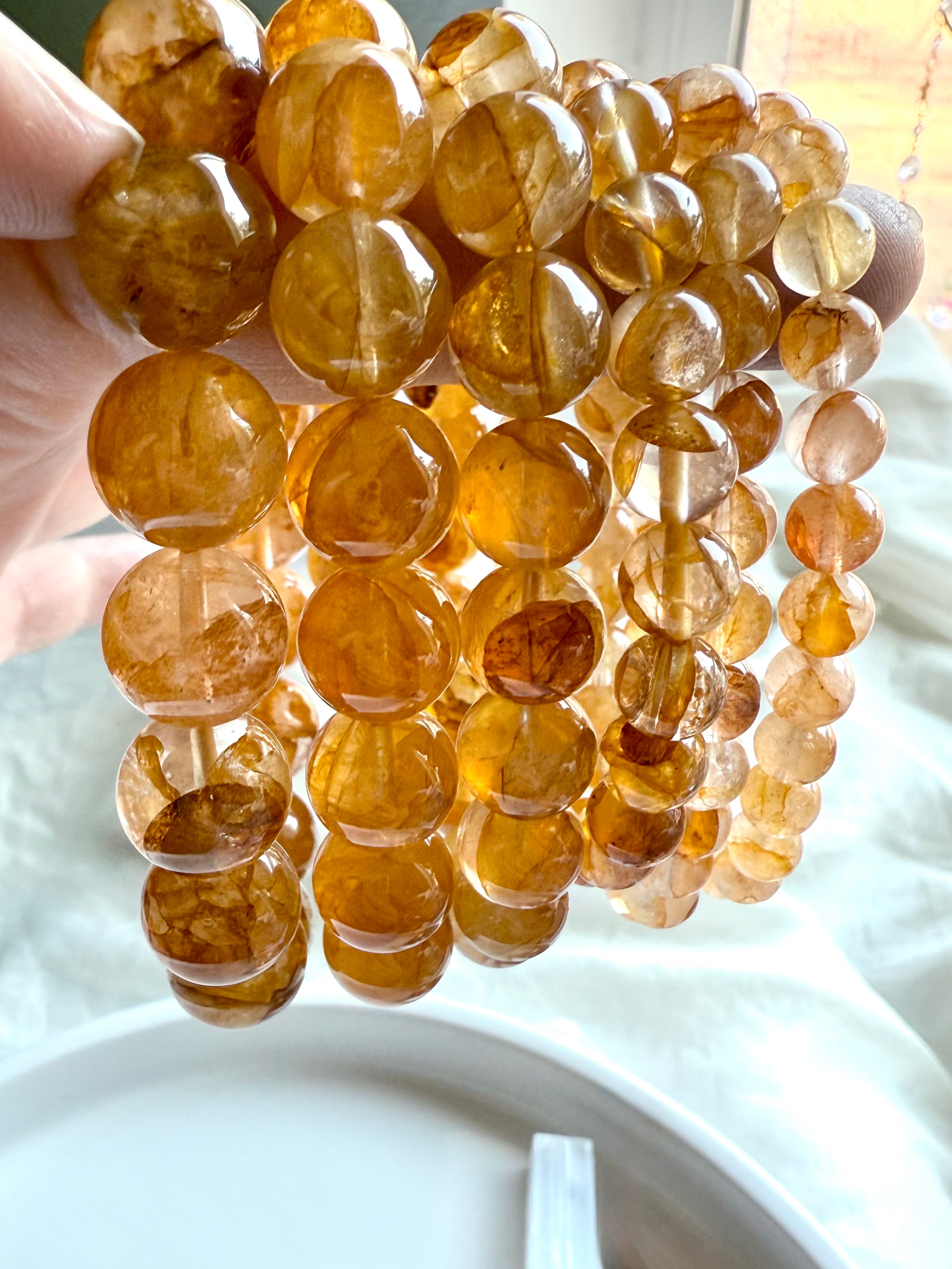 A row of six Golden Healer Quartz bracelets from large to small beads, held to the light to show luminous golden tones and natural clarity.