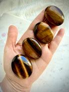 Hand holding polished Tiger’s Eye palm stones with rich golden flash and natural chatoyant bands 