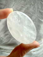 Clear Quartz palm stone held in hand showing wispy white veils and luminous internal patterns for clarity and meditation
