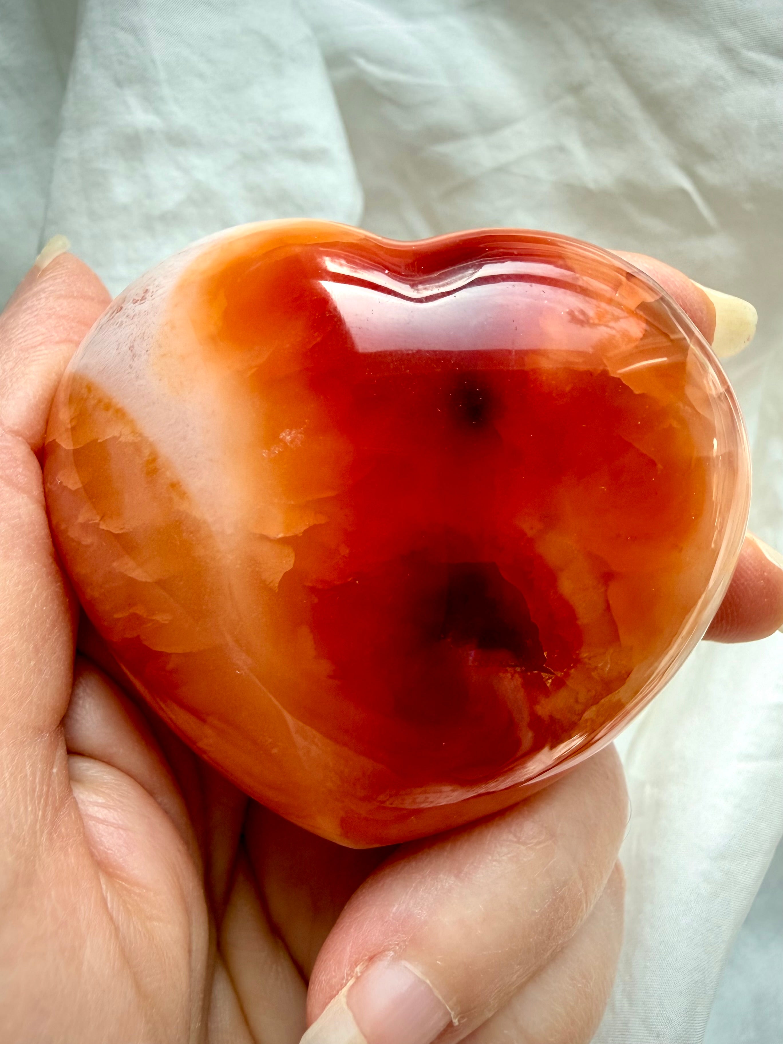 Close up of Carnelian heart crystal with translucent red and molten orange banding, natural inclusions, and high polish finish