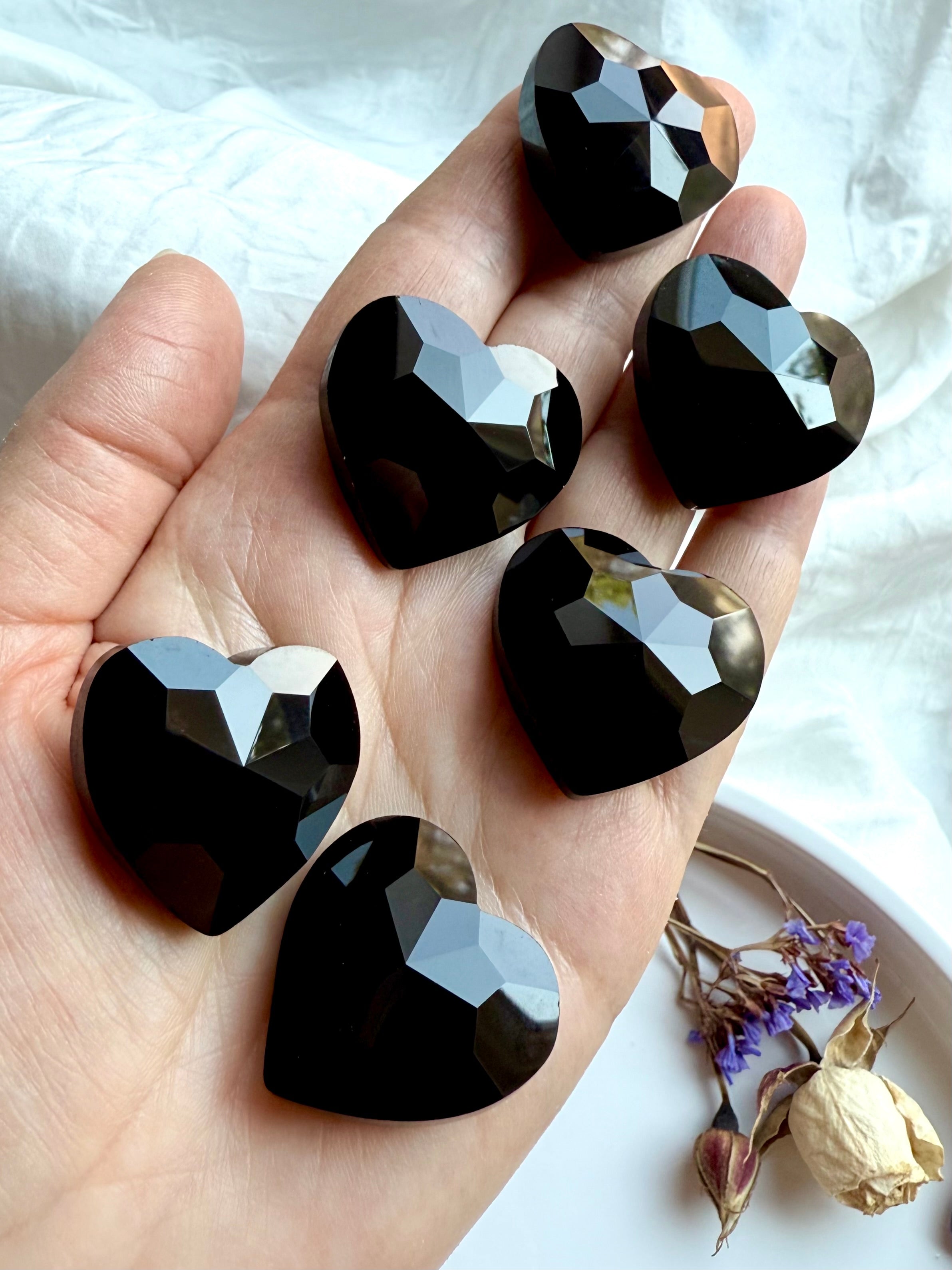 Hand holding black obsidian faceted crystal hearts for grounding and root chakra healing.