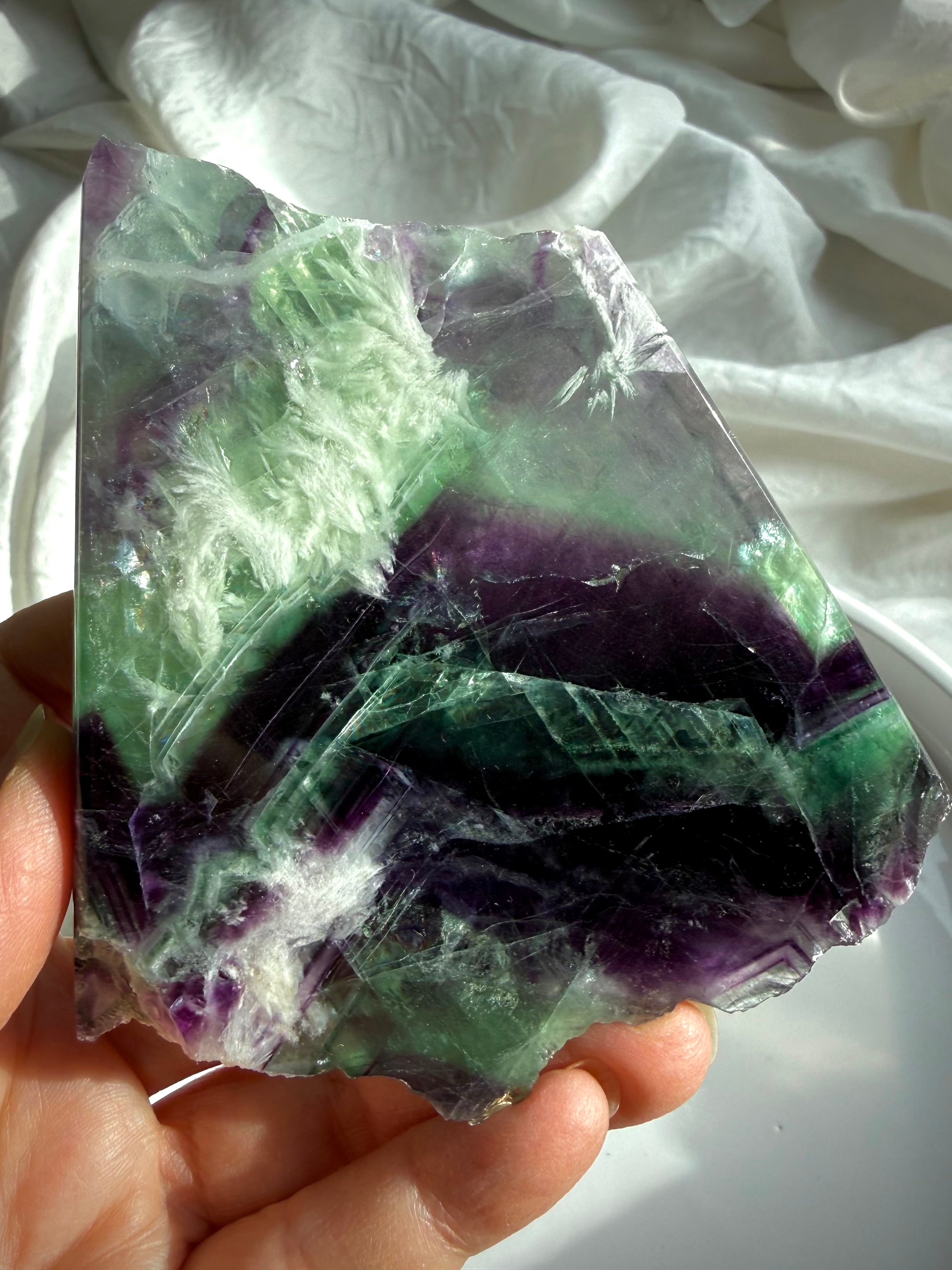 Polished fluorite slab photographed in natural light highlighting layered green and violet color zoning with rainbows