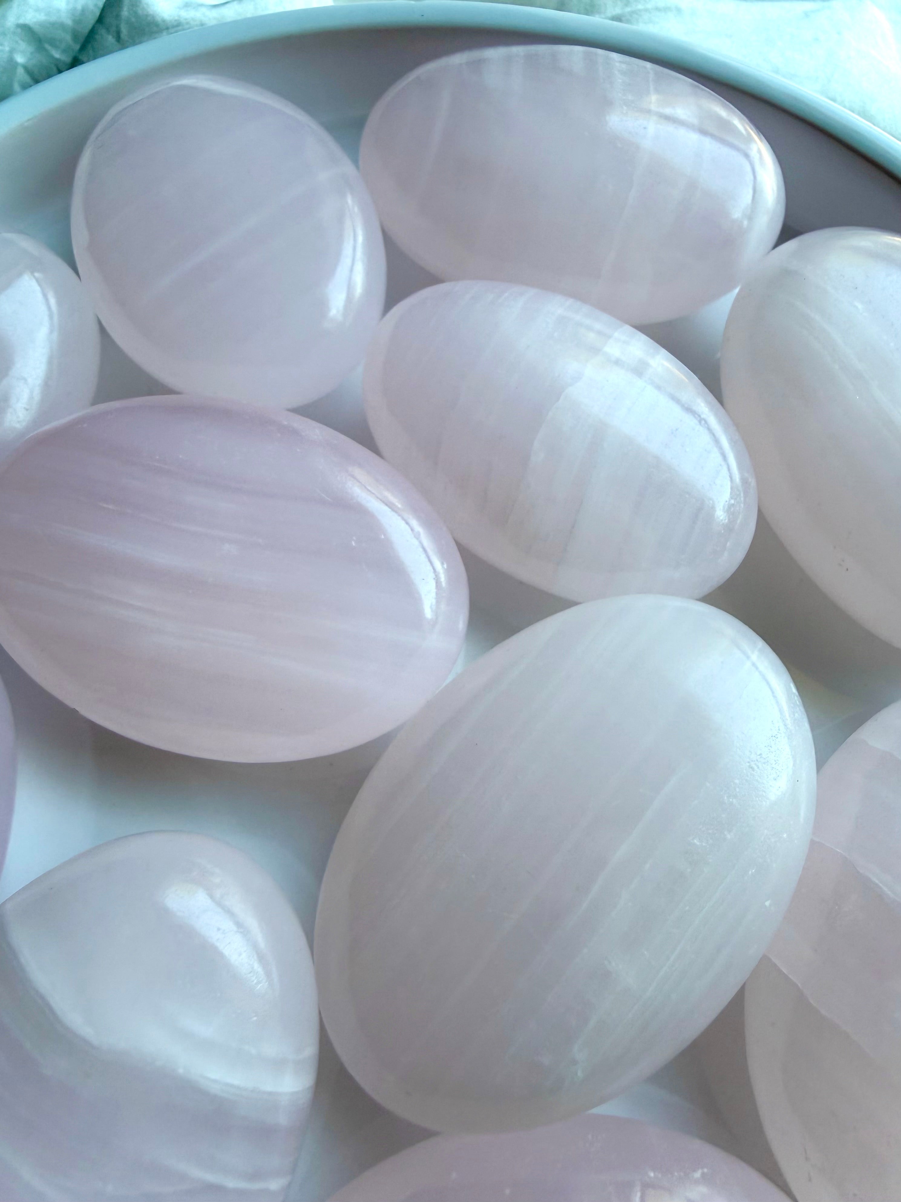 Polished Mangano Calcite palm stones displaying soft blush pink color and natural white banding