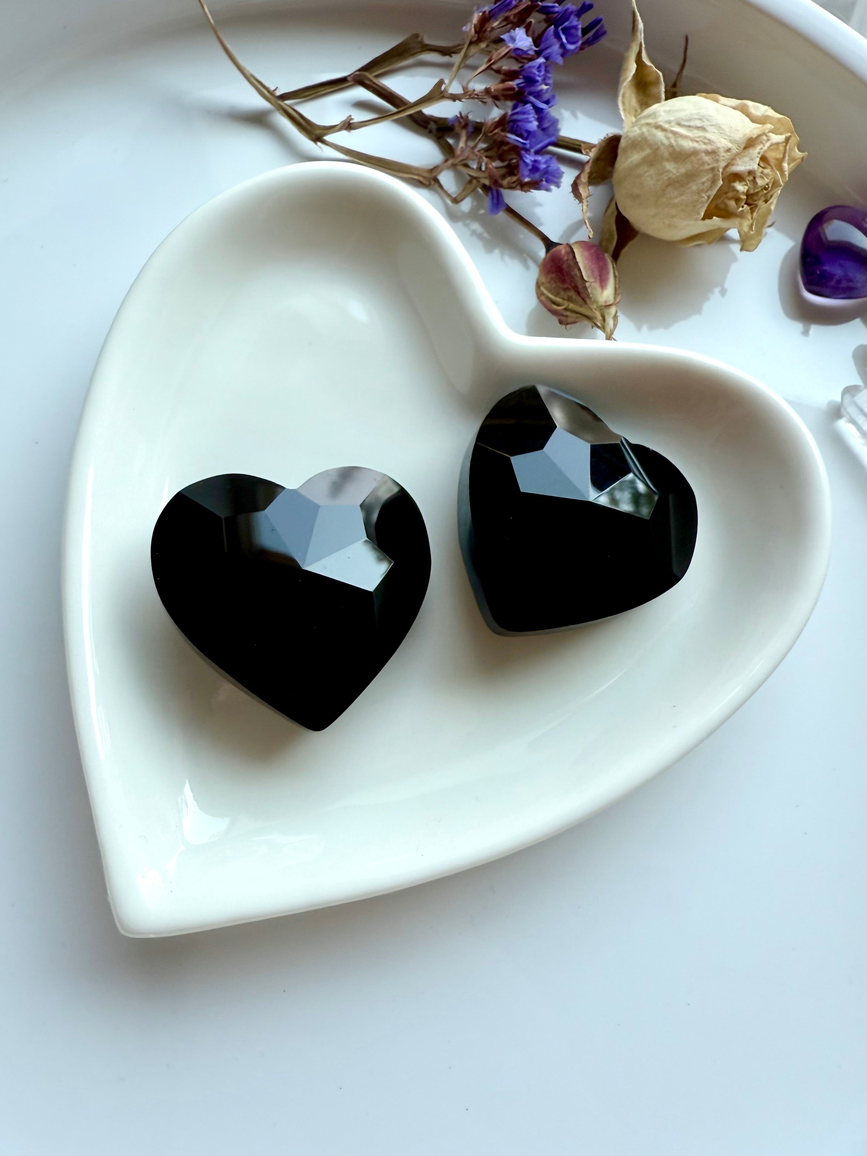 Black crystal hearts on a white heart-shaped dish with dried flowers in the background