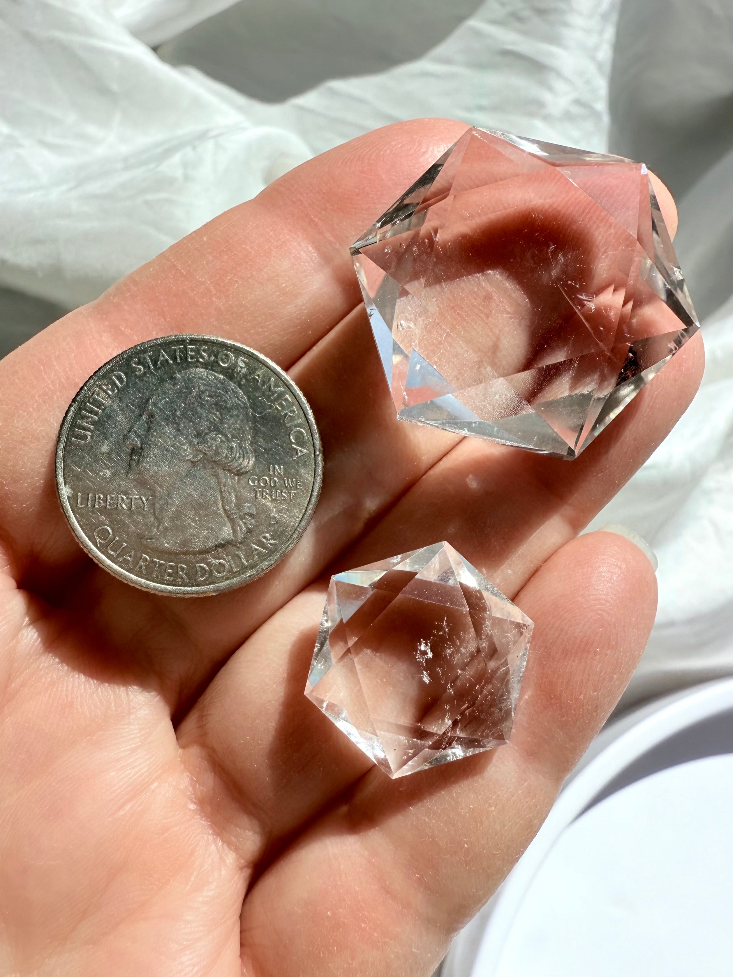Both sizes of faceted Clear Quartz hexagons shown on hand with quarter for scale reference