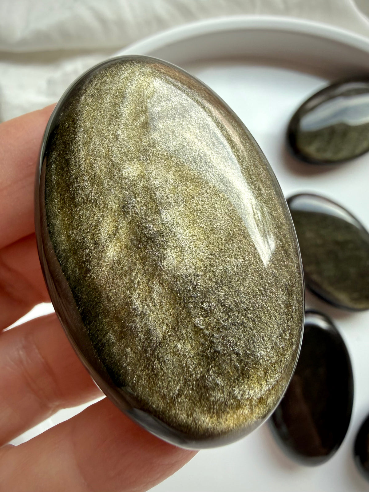 Golden Sheen Obsidian crystal held in hand showing strong metallic gold and bronze sheen across its glossy black surface