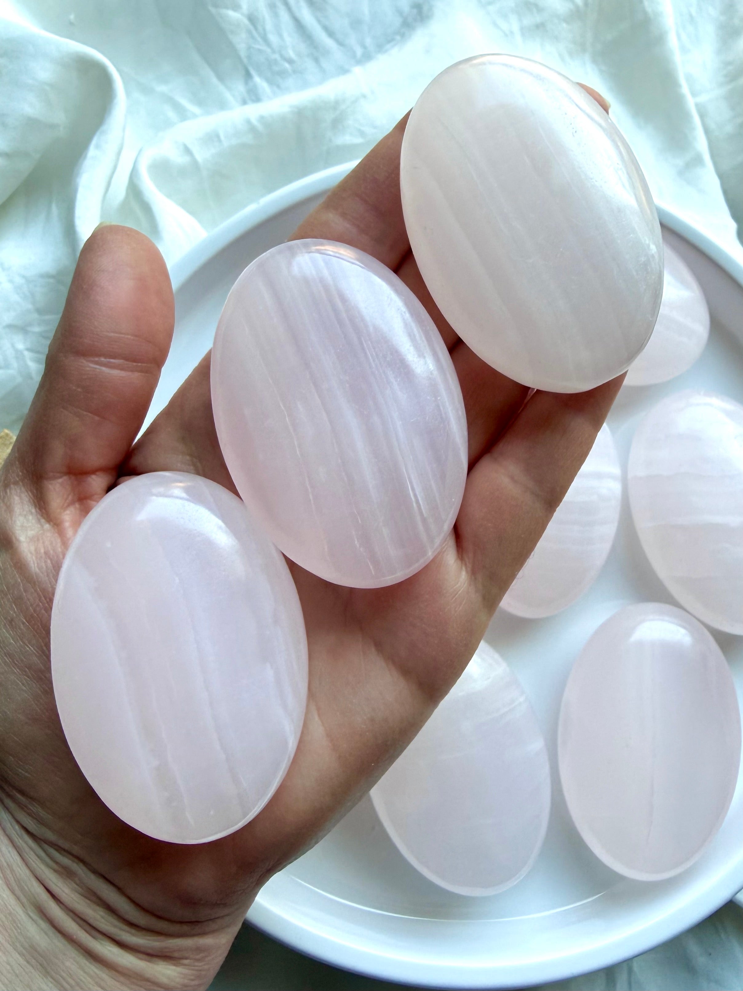 Assorted Mangano Calcite palm stones displayed on a white plate with natural pink banding and polished finish