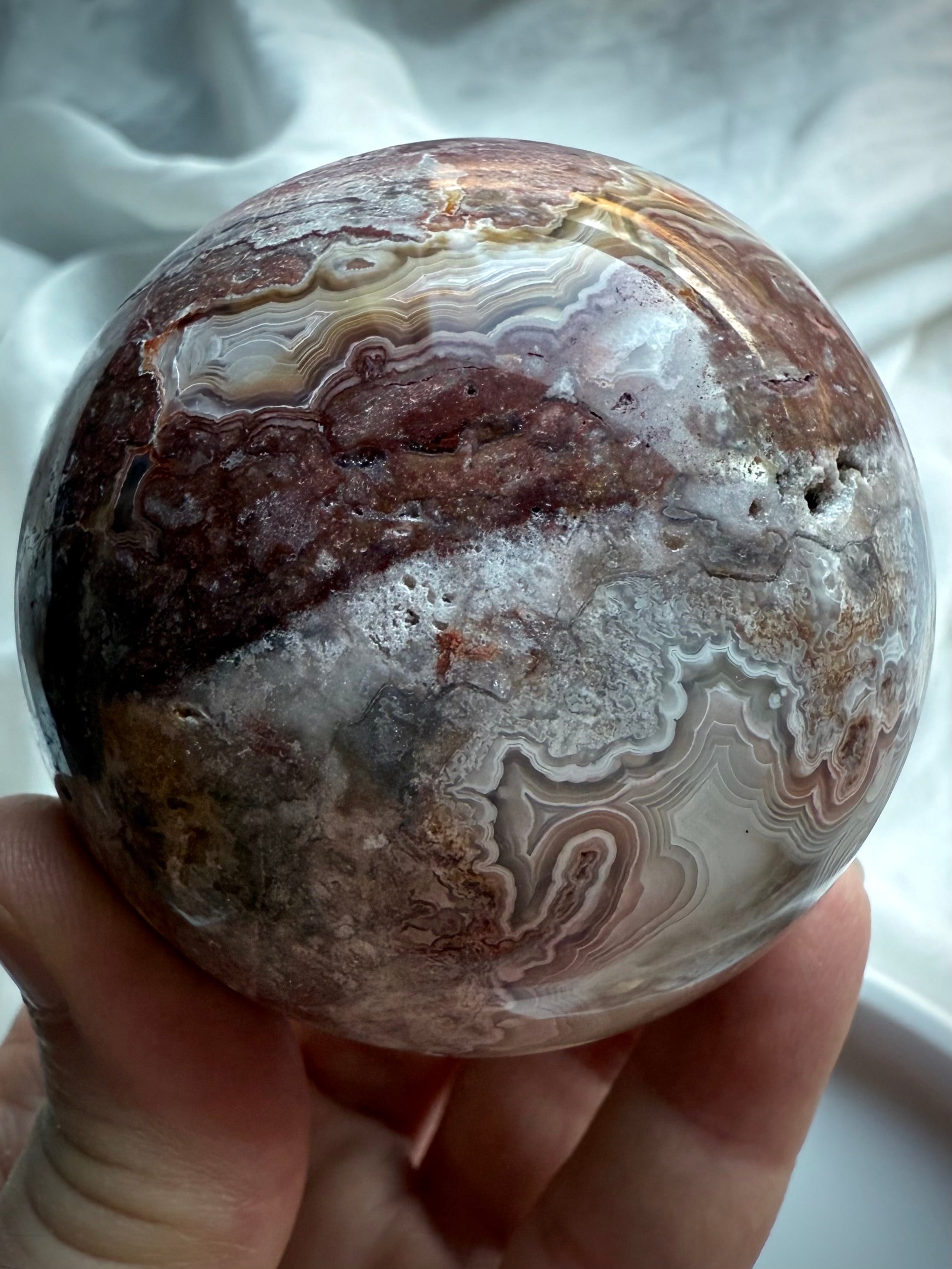 Polished gemstone sphere with swirling cream and plum-colored agate patterns and druzy crystal pocket