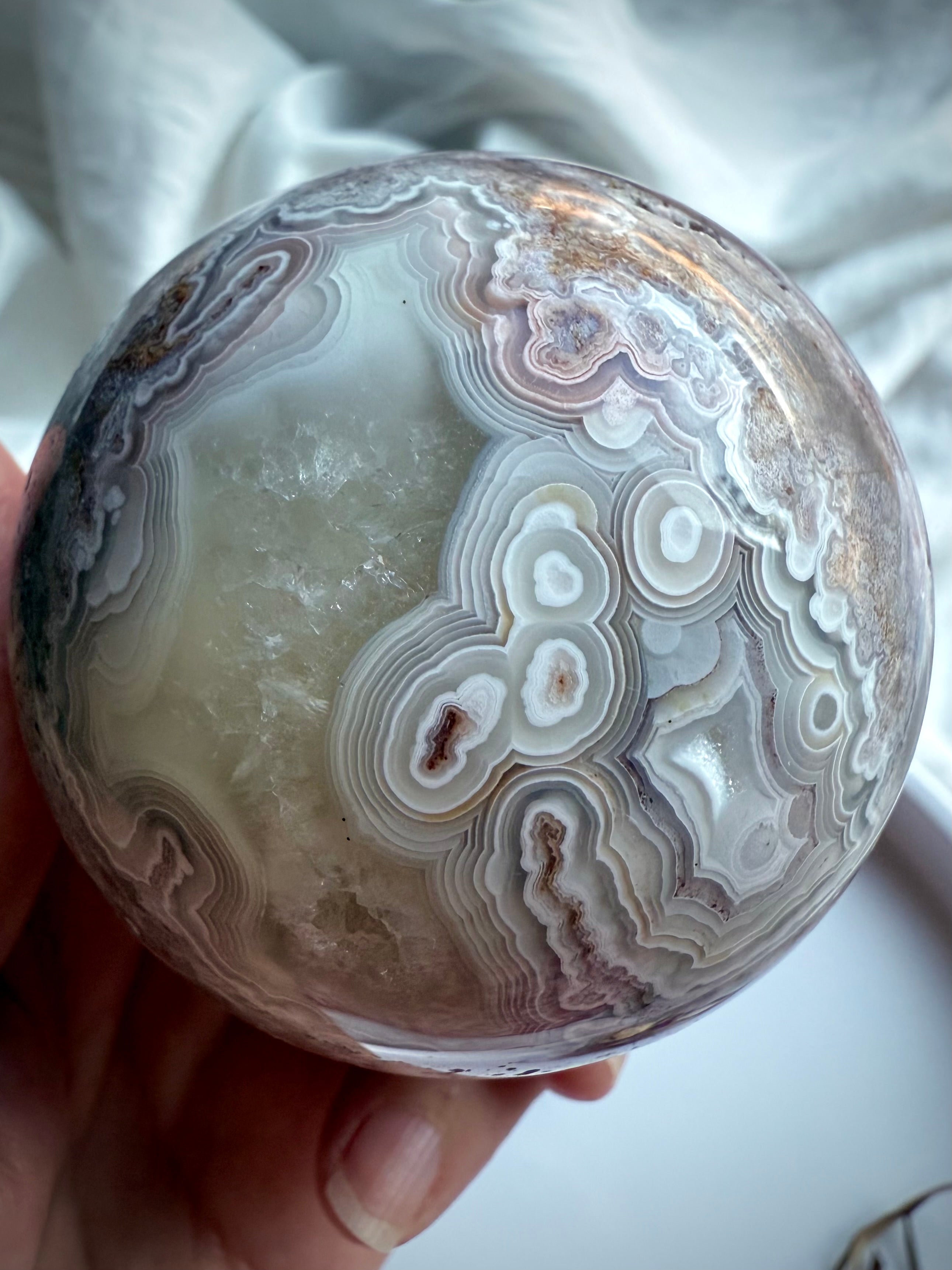 Crazy Lace Agate crystal sphere featuring bold circular banding, soft quartz druzy, and natural geological textures