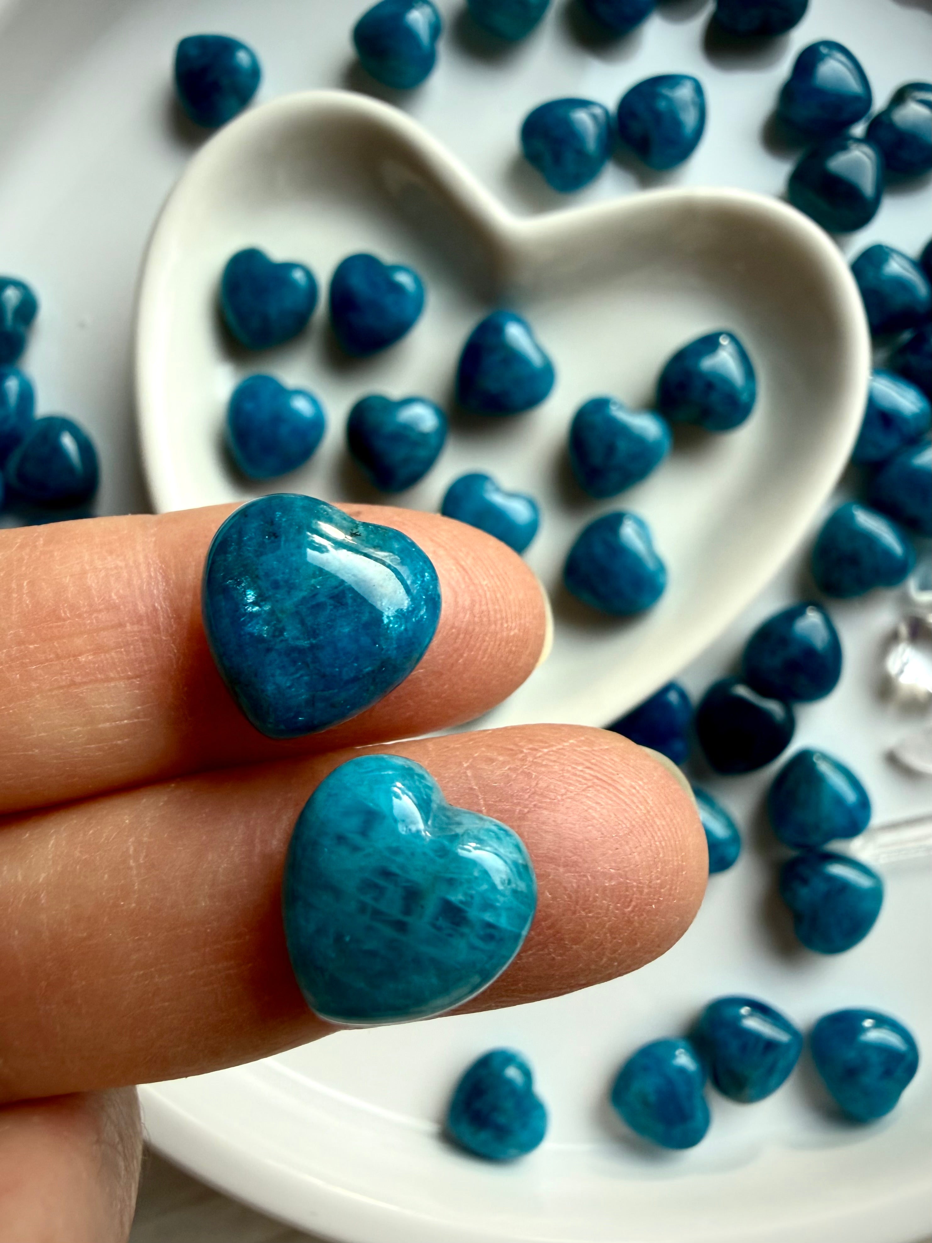 Mini Blue Apatite crystal heart held between fingers, showing glossy polish, rich blue color, and natural stone variation for size reference