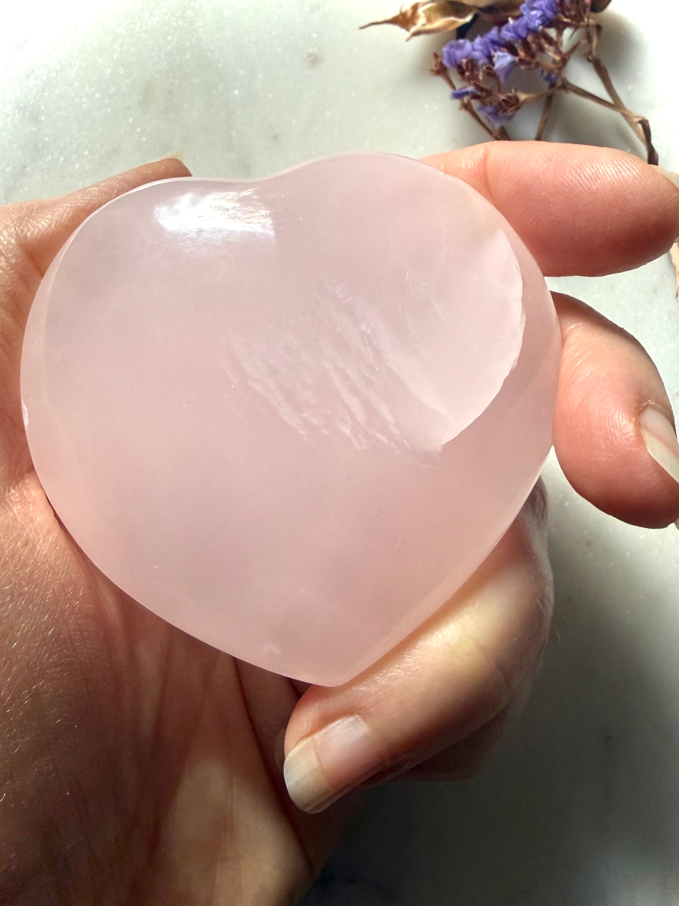 Palm sized Mangano Calcite heart crystal held in hand with soft blush pink color and subtle internal patterning