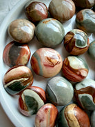 Assorted Polychrome Jasper mini palm stones in a white bowl, featuring warm rust, sage green, cream, and gray mineral patterns