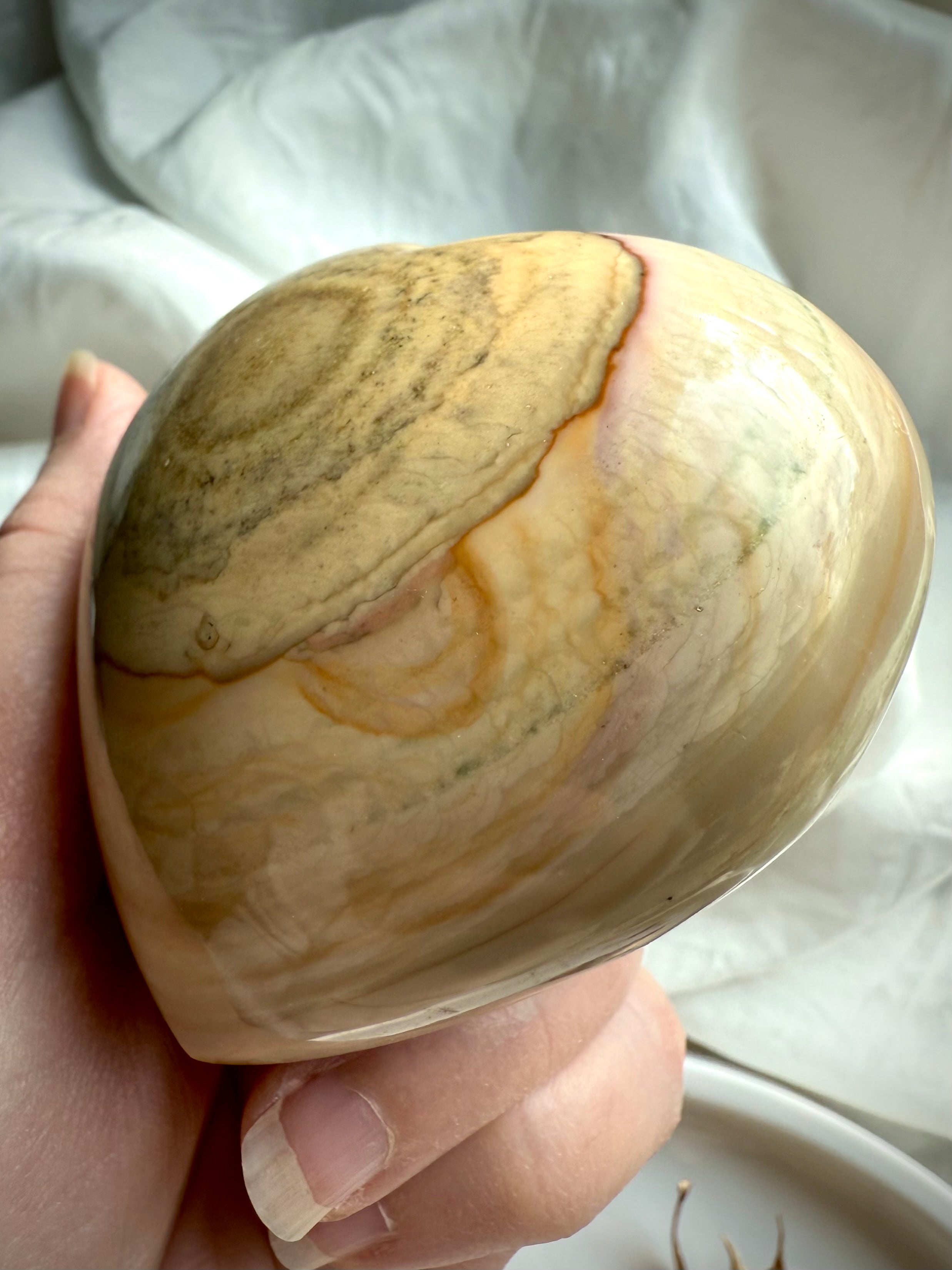 Polished Ocean Jasper heart with soft beige, tan, and cream banding held in hand — grounding healing stone for comfort, love, and emotional balance.