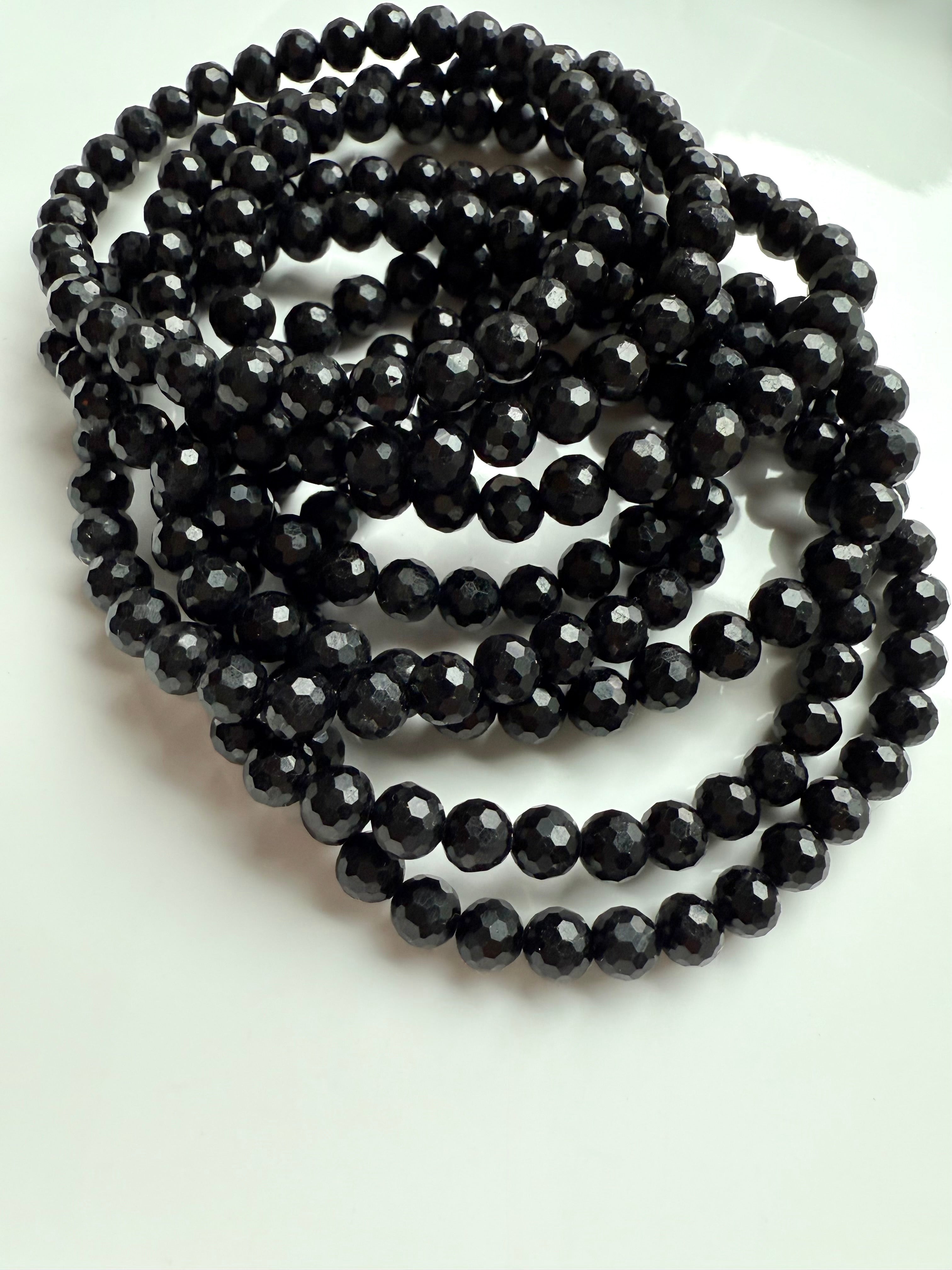 pile of faceted black tourmaline stretch bracelets coiled on white dish, ready for crystal protection ritual
