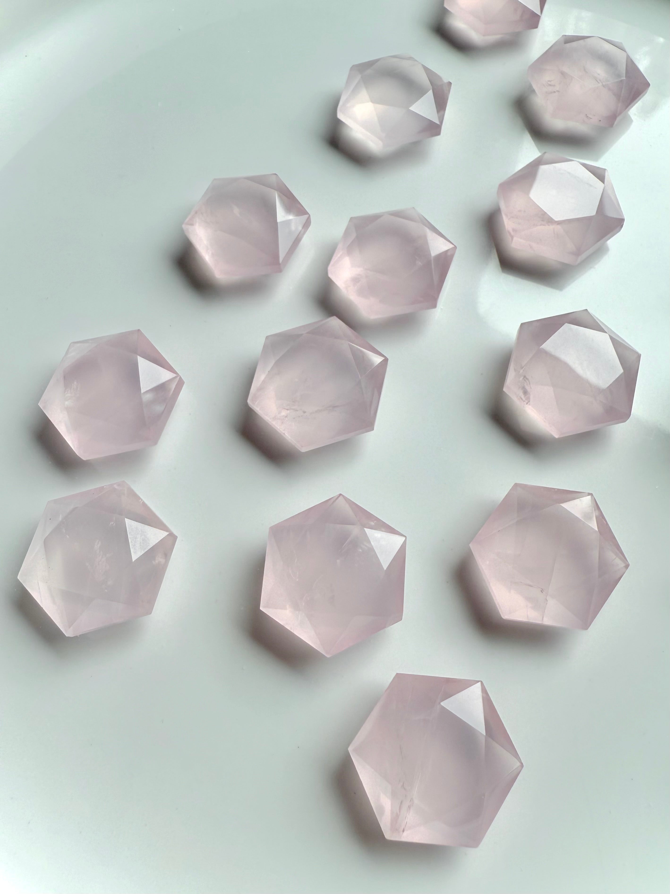 Several faceted rose quartz hexagons on white, mini-sized Heart Chakra crystals with natural veining & soft pink color