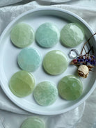 Eight round Pistachio Calcite crystal palm stones displayed in a white tray – heart chakra meditation tools for calm, clarity, and emotional support