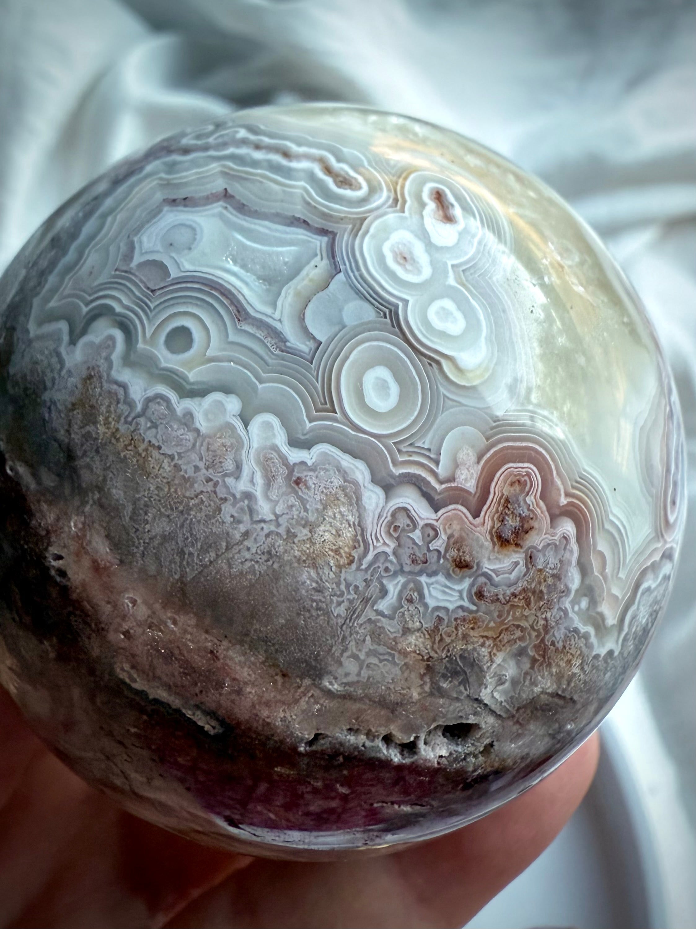 Close-up of intricate pink, lilac, and ivory agate banding with orbicular patterns on polished crystal sphere