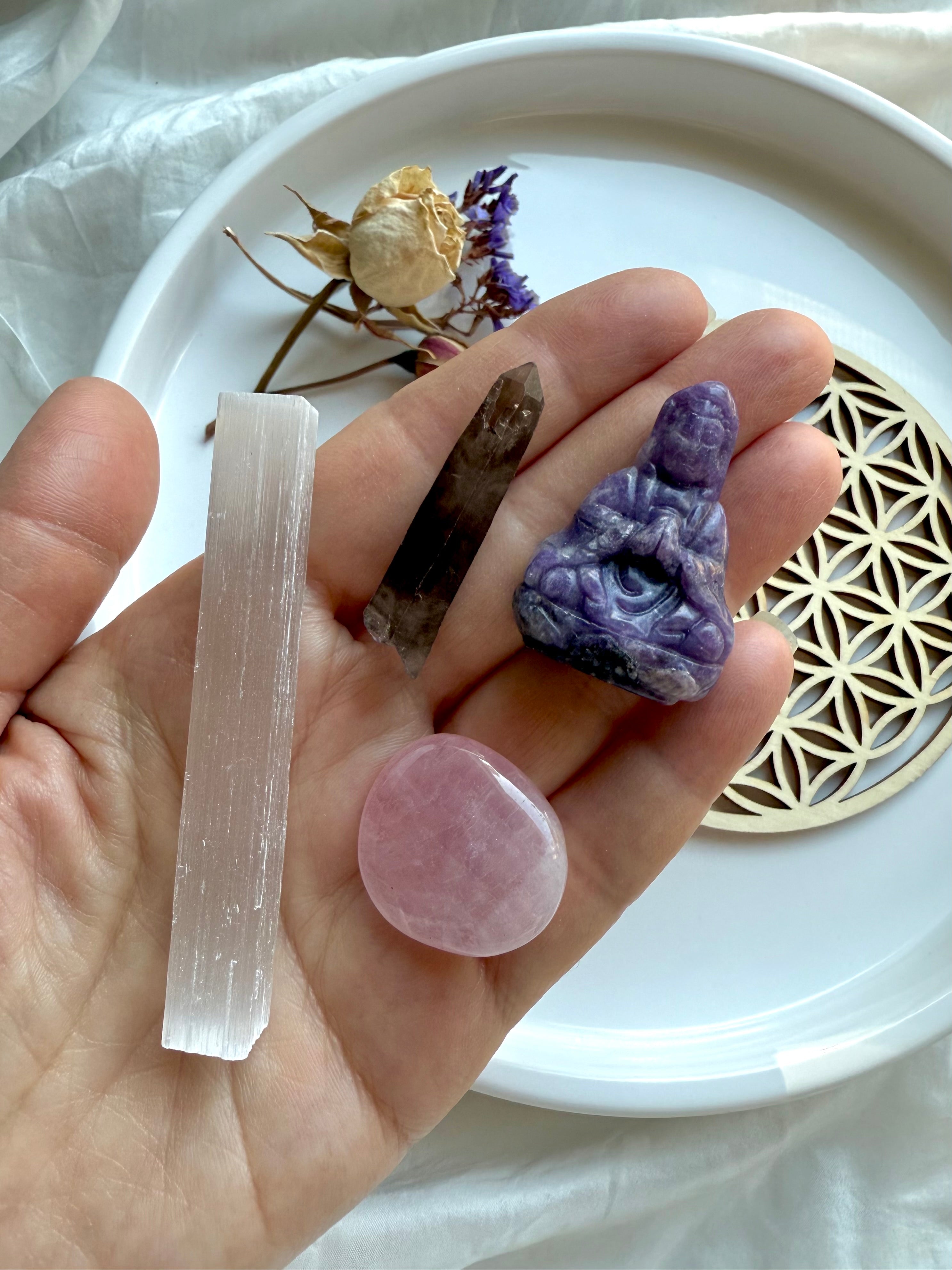 Hand holding Lepidolite Quan Yin, rose quartz, smoky quartz + selenite – components of the Quan Yin Travel Altar Crystal Gift Set for serenity, clearing + heart healing