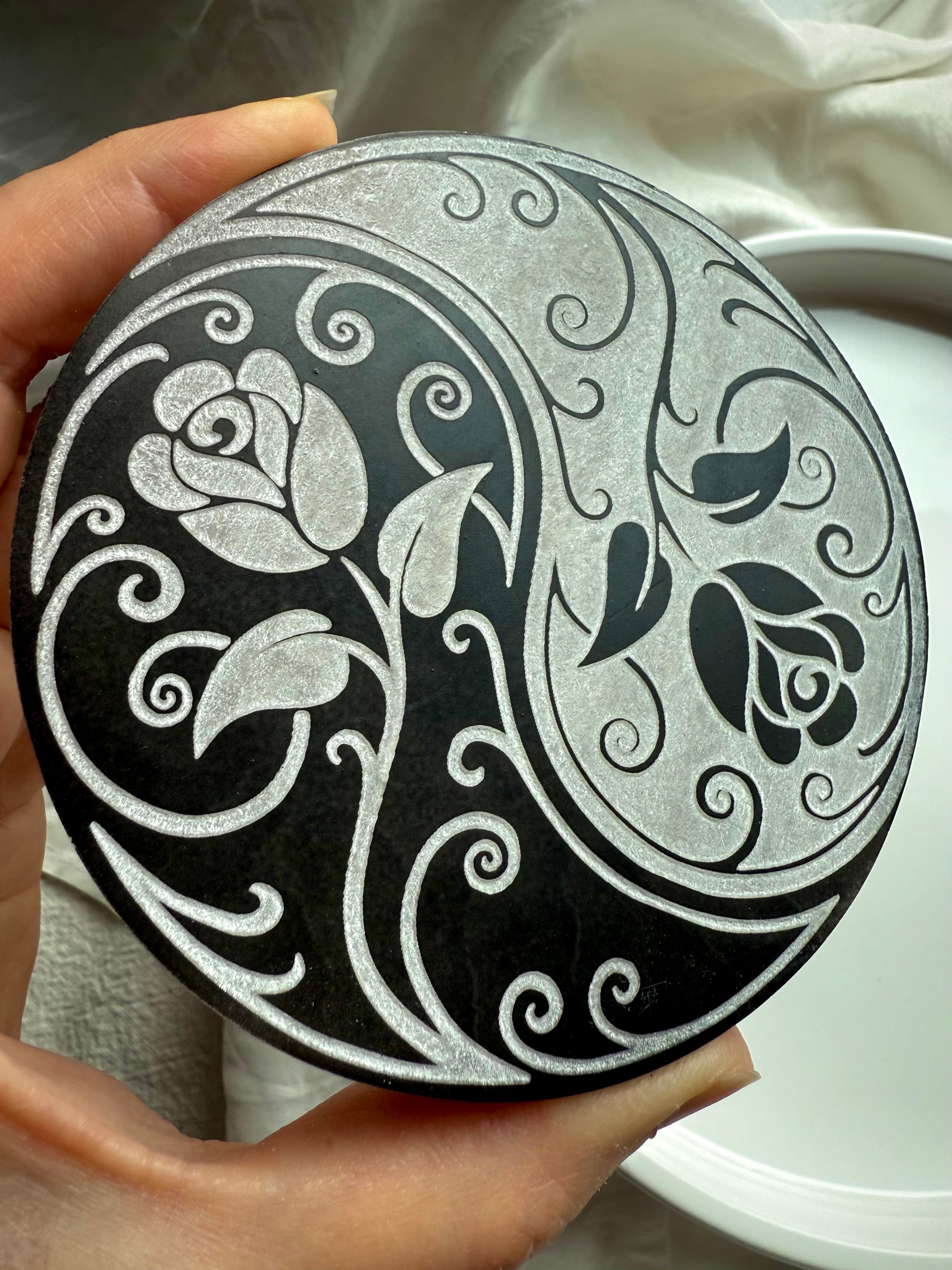Hand holding yin yang rose selenite charging plate showing carved floral design for spiritual energy clearing 