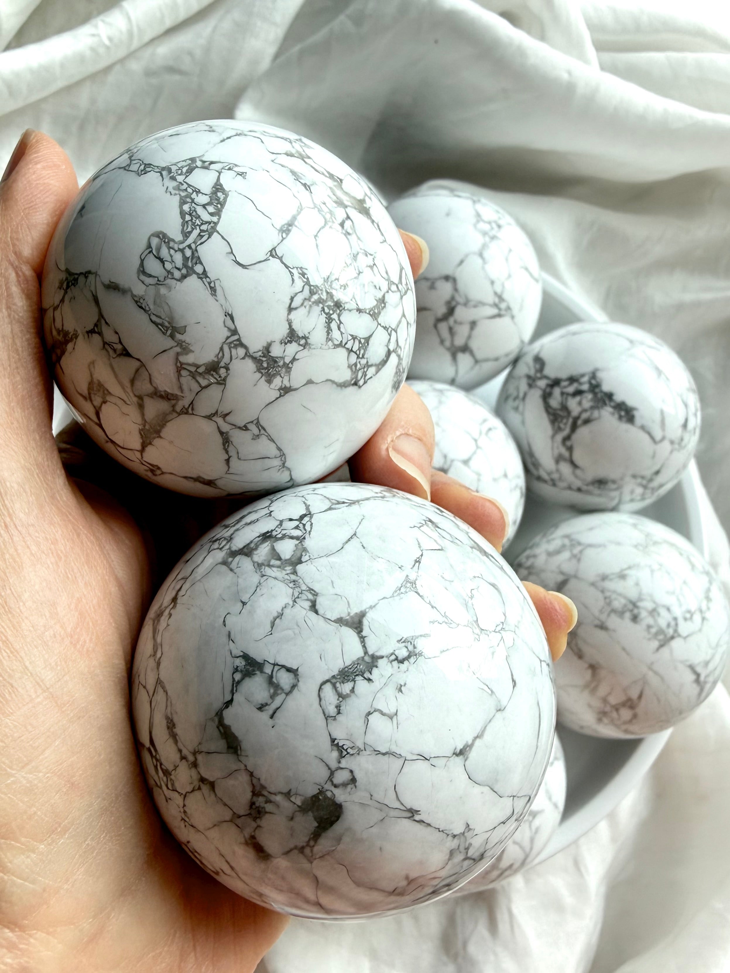 Closeup of two Howlite spheres in hand for size reference, polished white stone with gray marbling for calm and stress relief