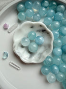 Polished Aquamarine sphere in soft ocean blue – mini March birthstone crystals styled in marble bowl