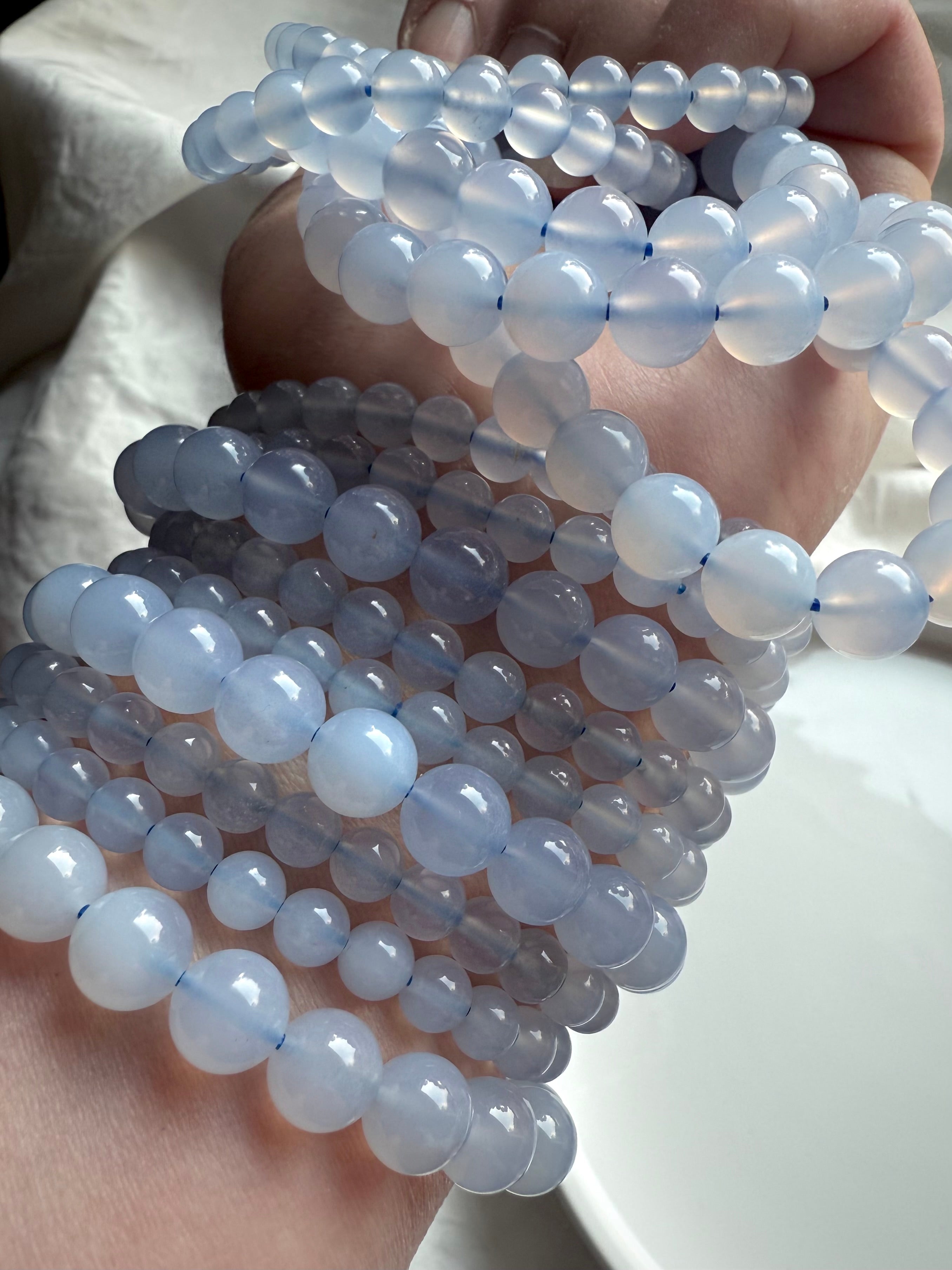 Multiple Blue Chalcedony crystal bead bracelets layered on arm — polished translucent blue gemstones for peace and emotional healing.