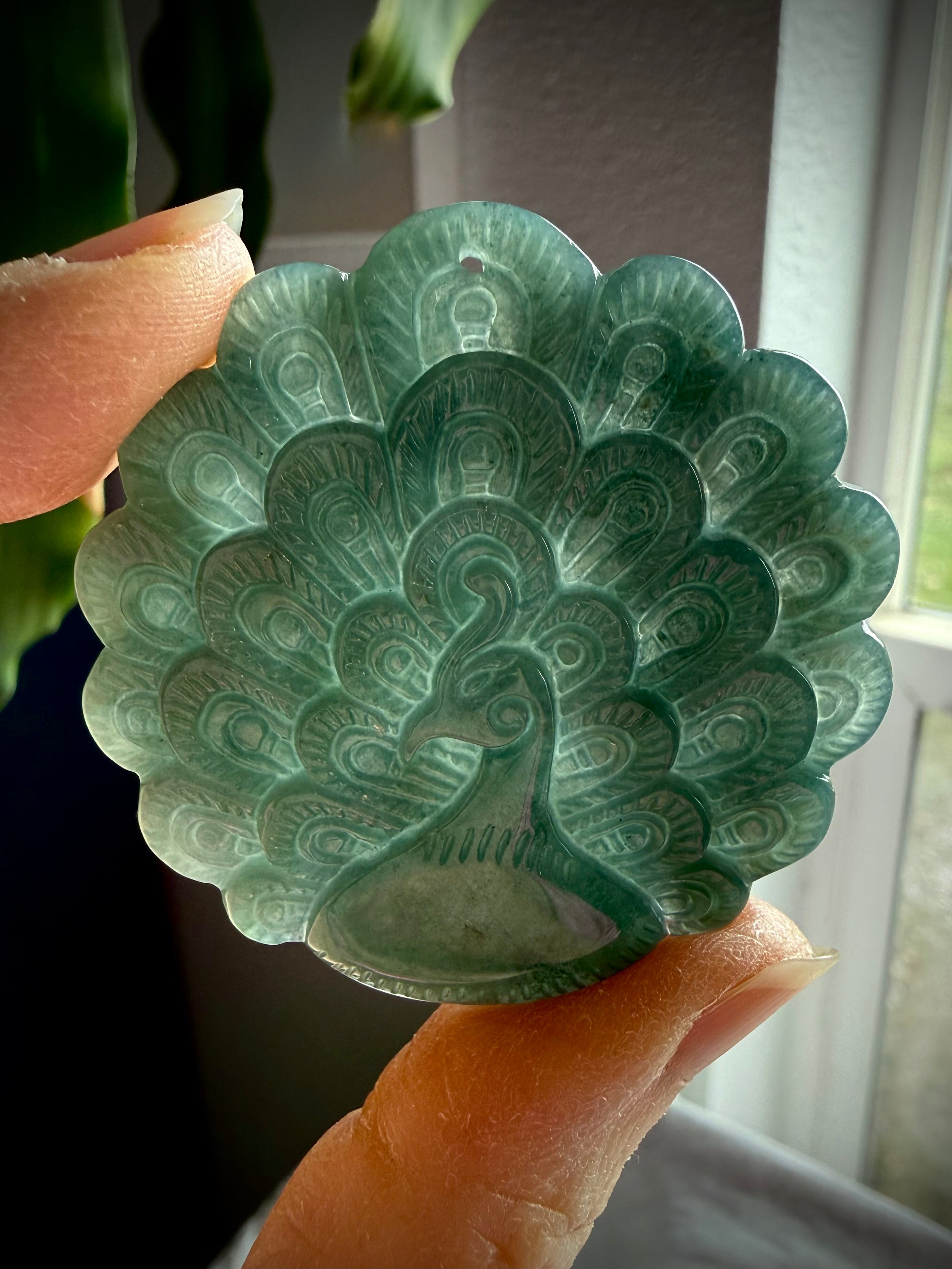 Blue Water Jade peacock medallion held to the light showing lovely translucence and rich blue-green color