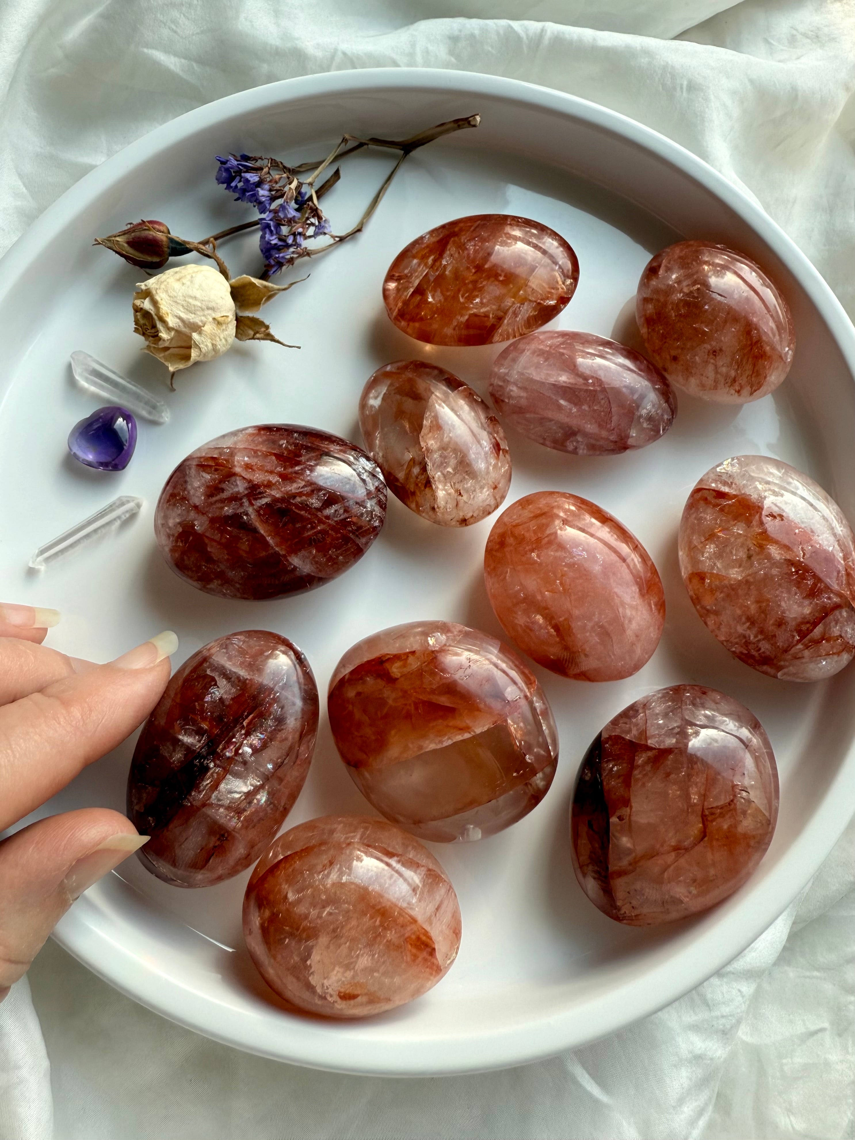 Fire Quartz palm stones with red and golden hematite inclusions displayed in a white dish for Root and Solar Plexus Chakra healing