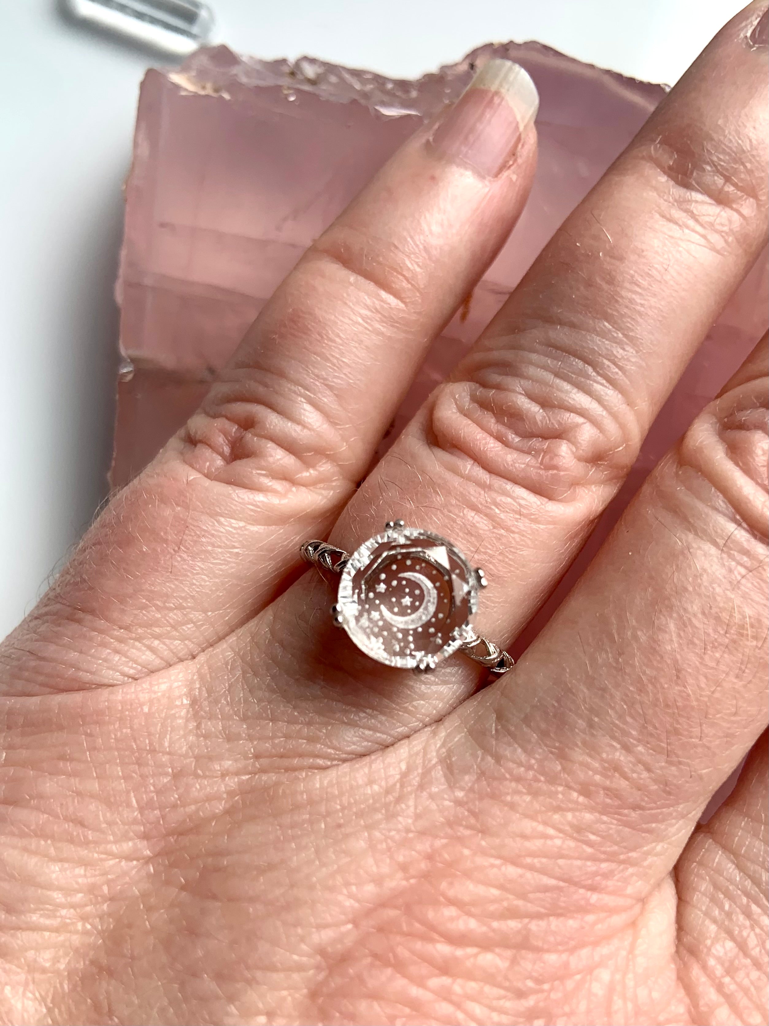 Hand holding Clear Quartz Moon Ring showing sparkling etched crescent and stars in round faceted gemstone, solitaire setting in sterling silver