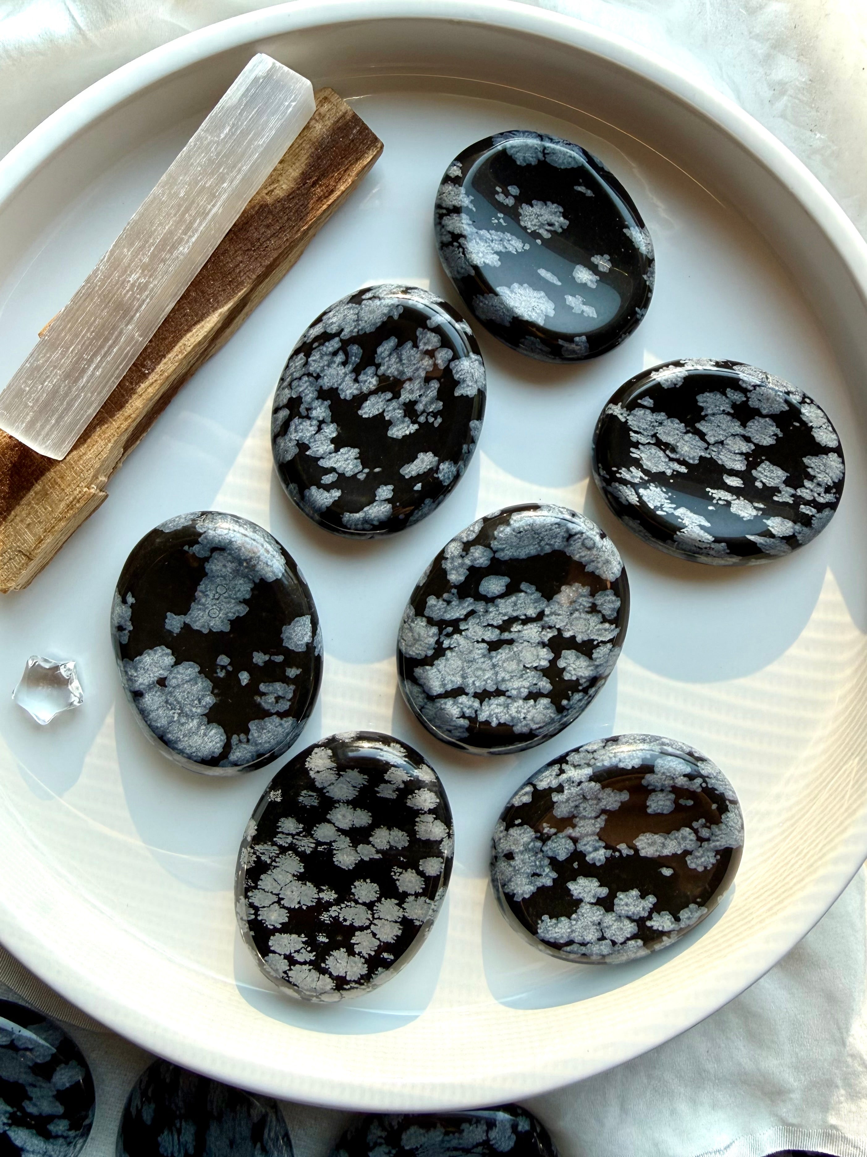 Snowflake Obsidian worry stones with silver crystal patterns on white ceramic plate for grounding and stress relief