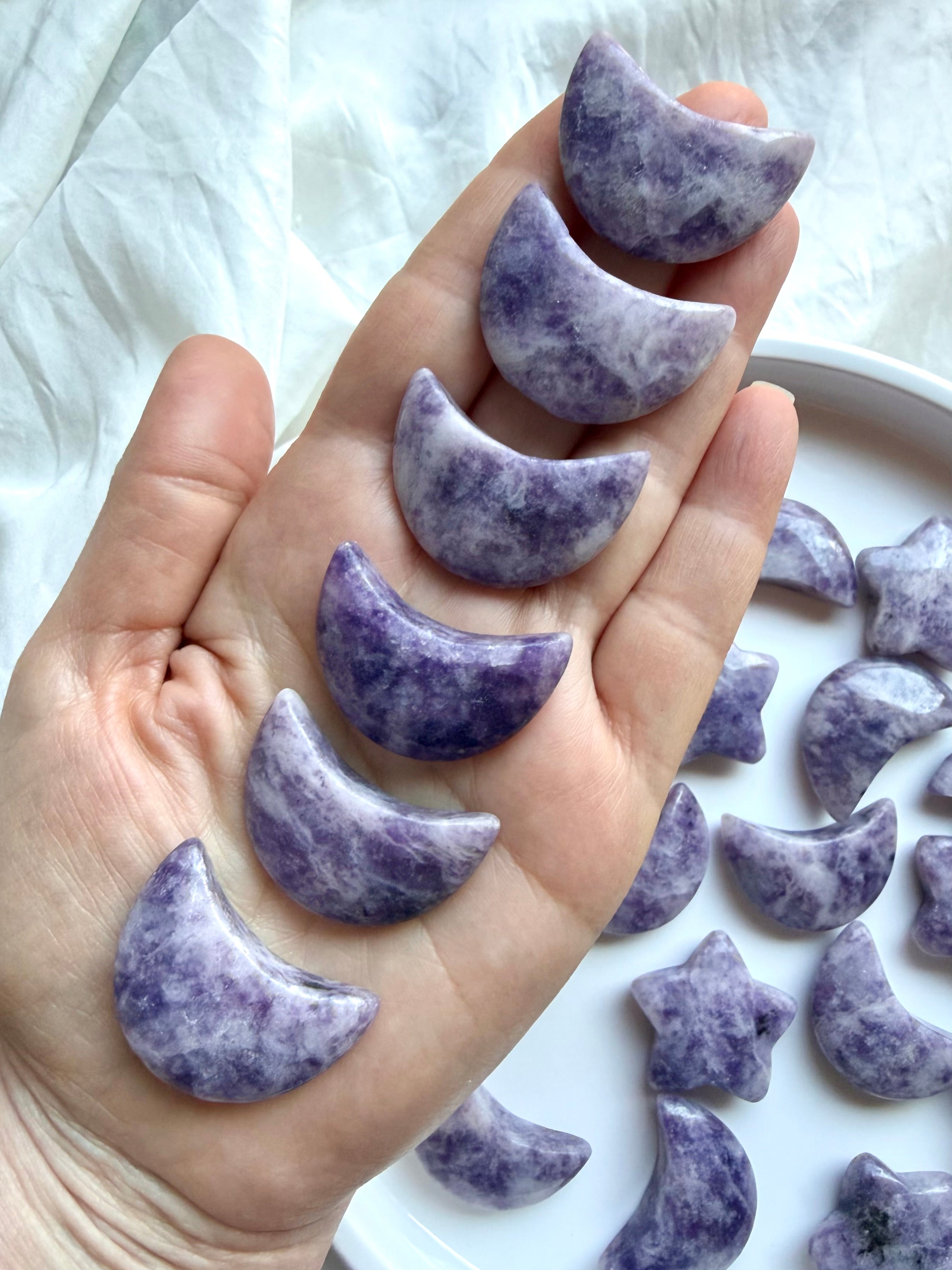 Lepidolite crescent moon crystal carvings held in hand showing natural lilac, lavender and deep purple variation