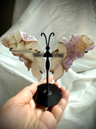 Druzy amethyst butterfly wings on metal stand held in hand, showing size and carved agate details.

