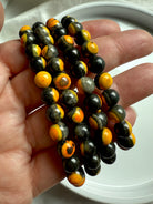 Tight close-up of polished bumblebee jasper beads showing natural mineral layering in vibrant solar plexus tones of black, gold, and orange