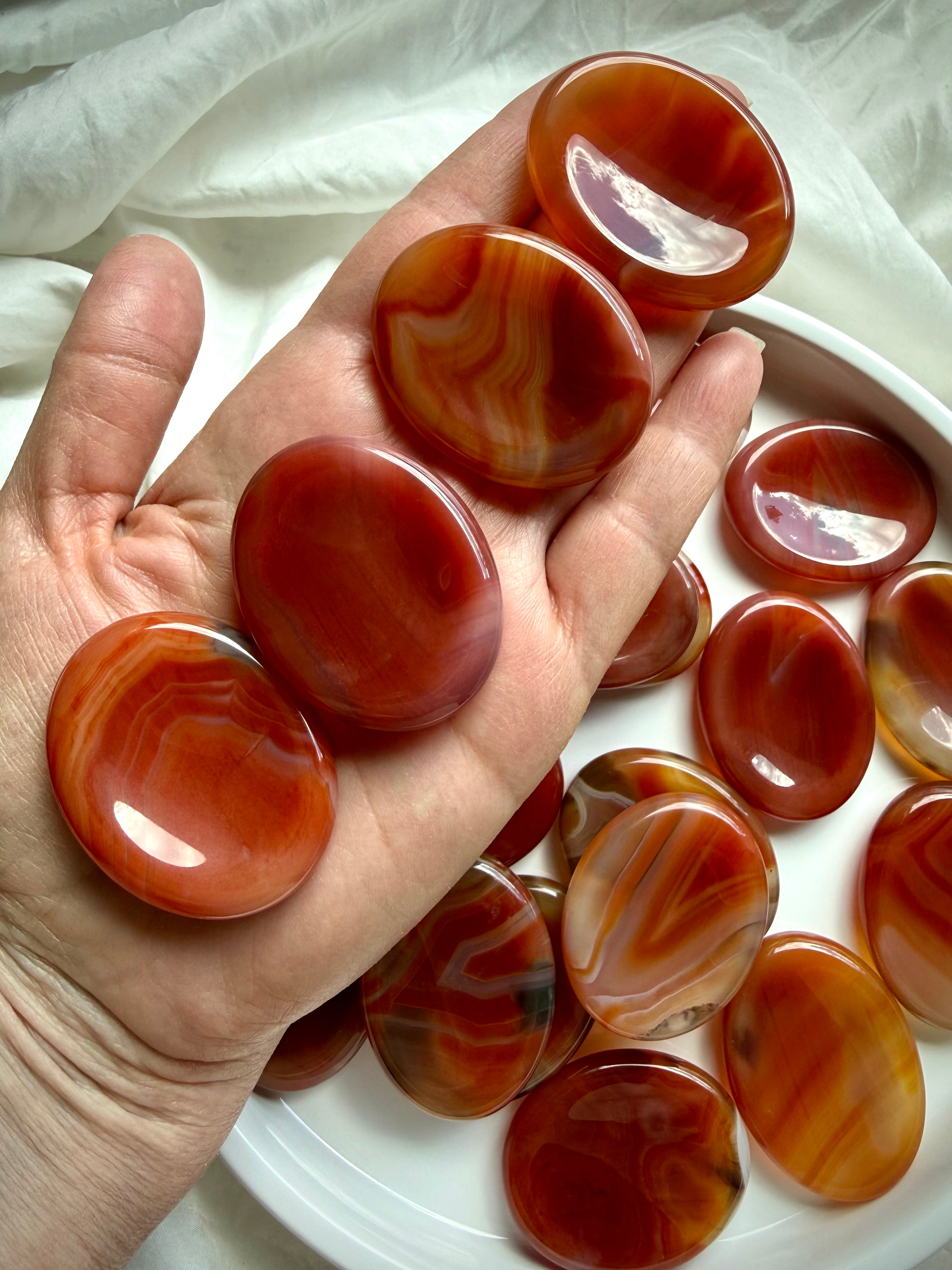 Carnelian worry stones held in hand, polished red-orange thumb stones for confidence, motivation and stress relief